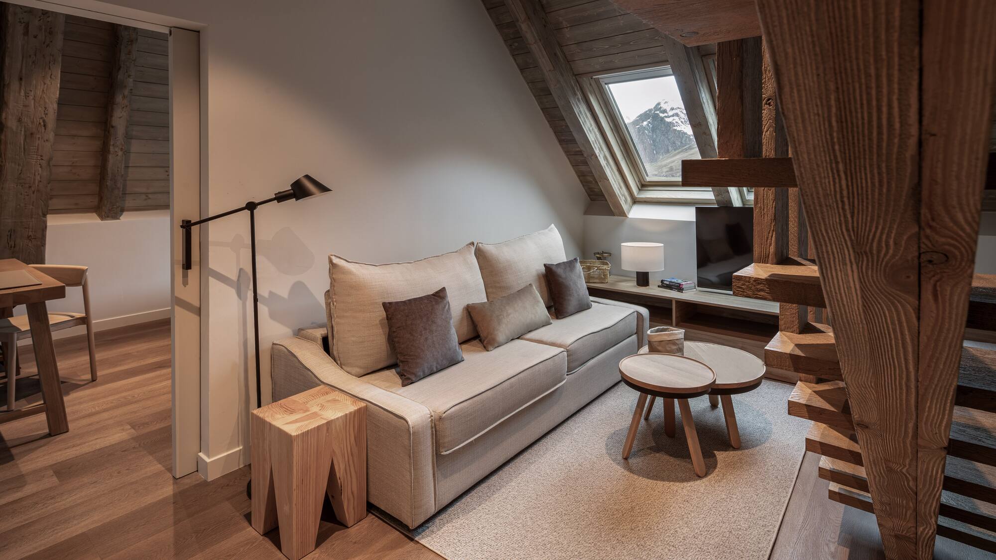 Cozy living room, sofa, wooden beams, and mountain view from attic window.