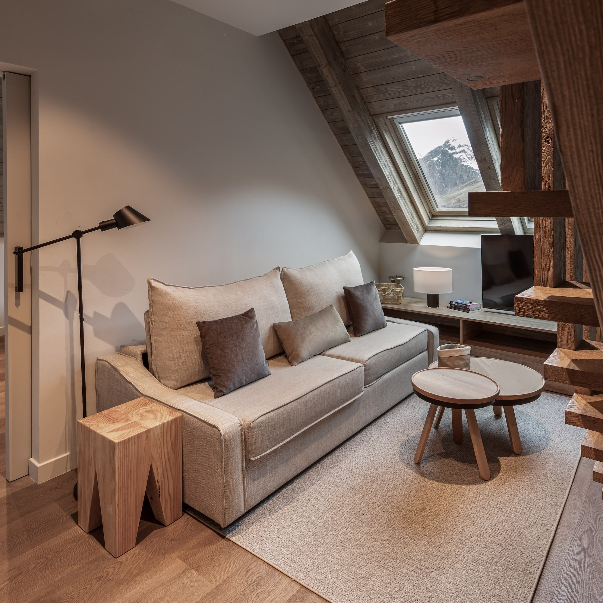 Cozy living room, sofa, wooden beams, and mountain view from attic window.