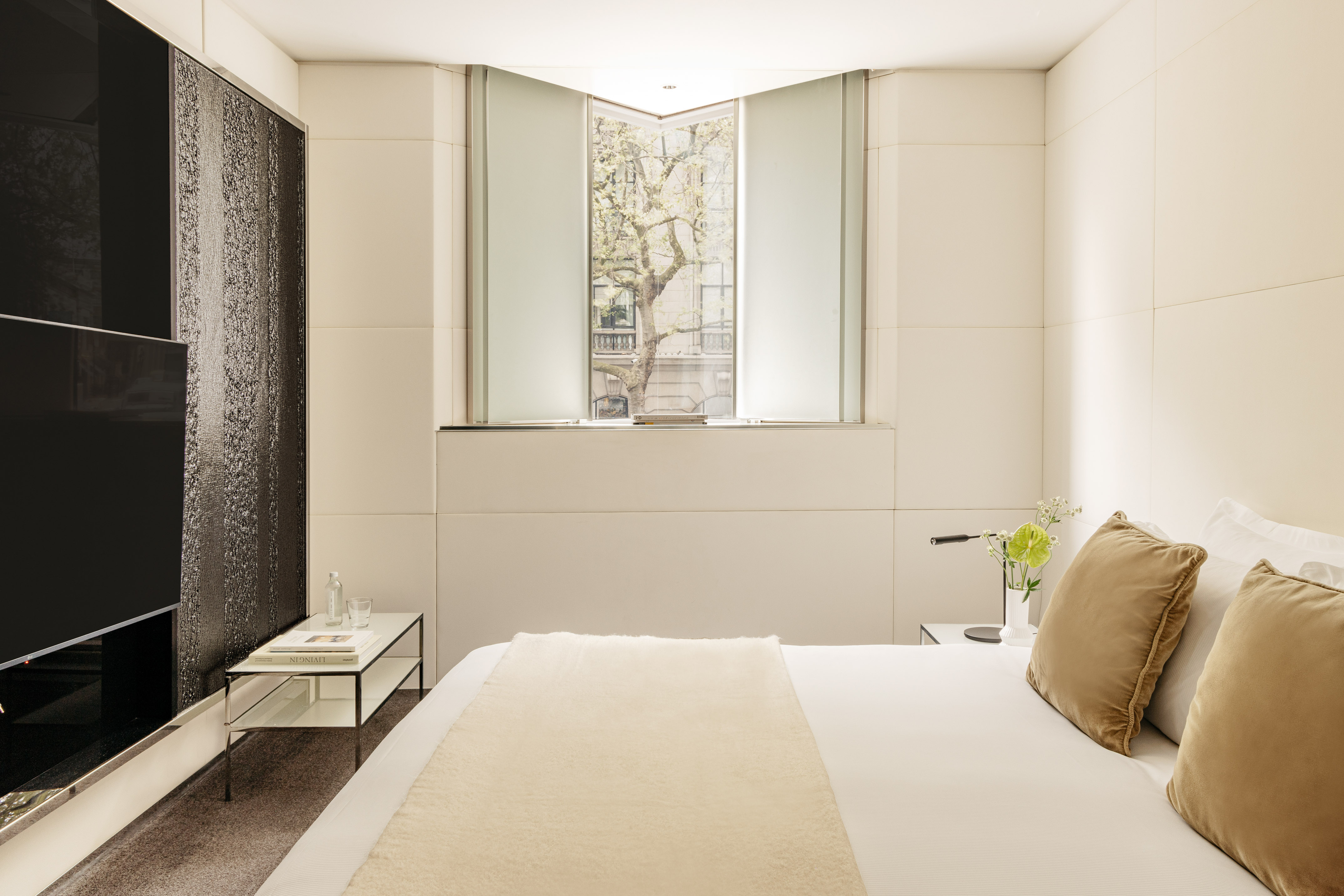 Luxury hotel bedroom with cream decor, modern bed, and window tree view.