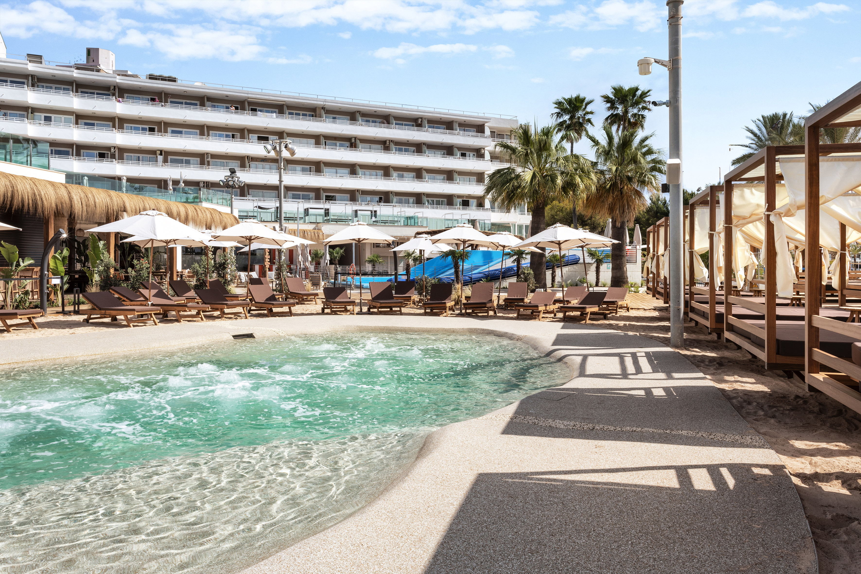Hotel poolside with turquoise water, sun loungers, and beach cabanas.