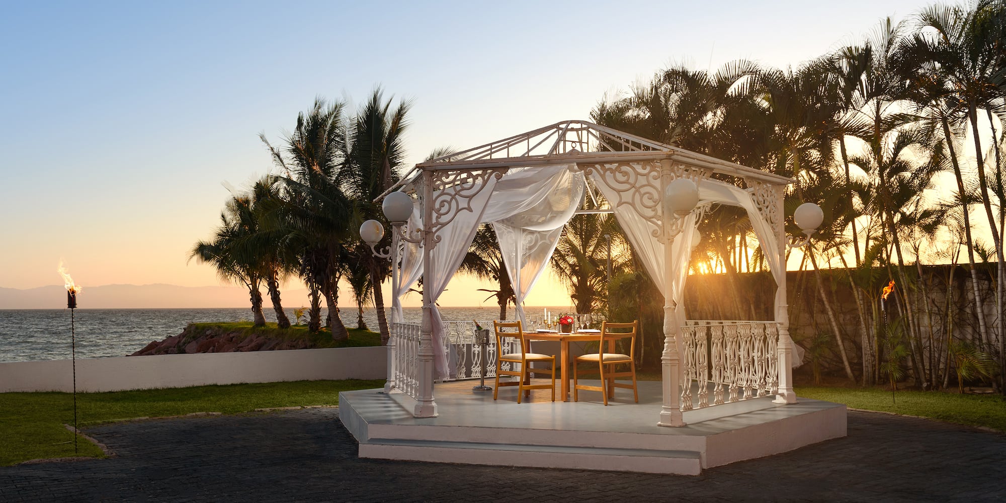 a white gazebo with a table and chairs on a patio with palm trees