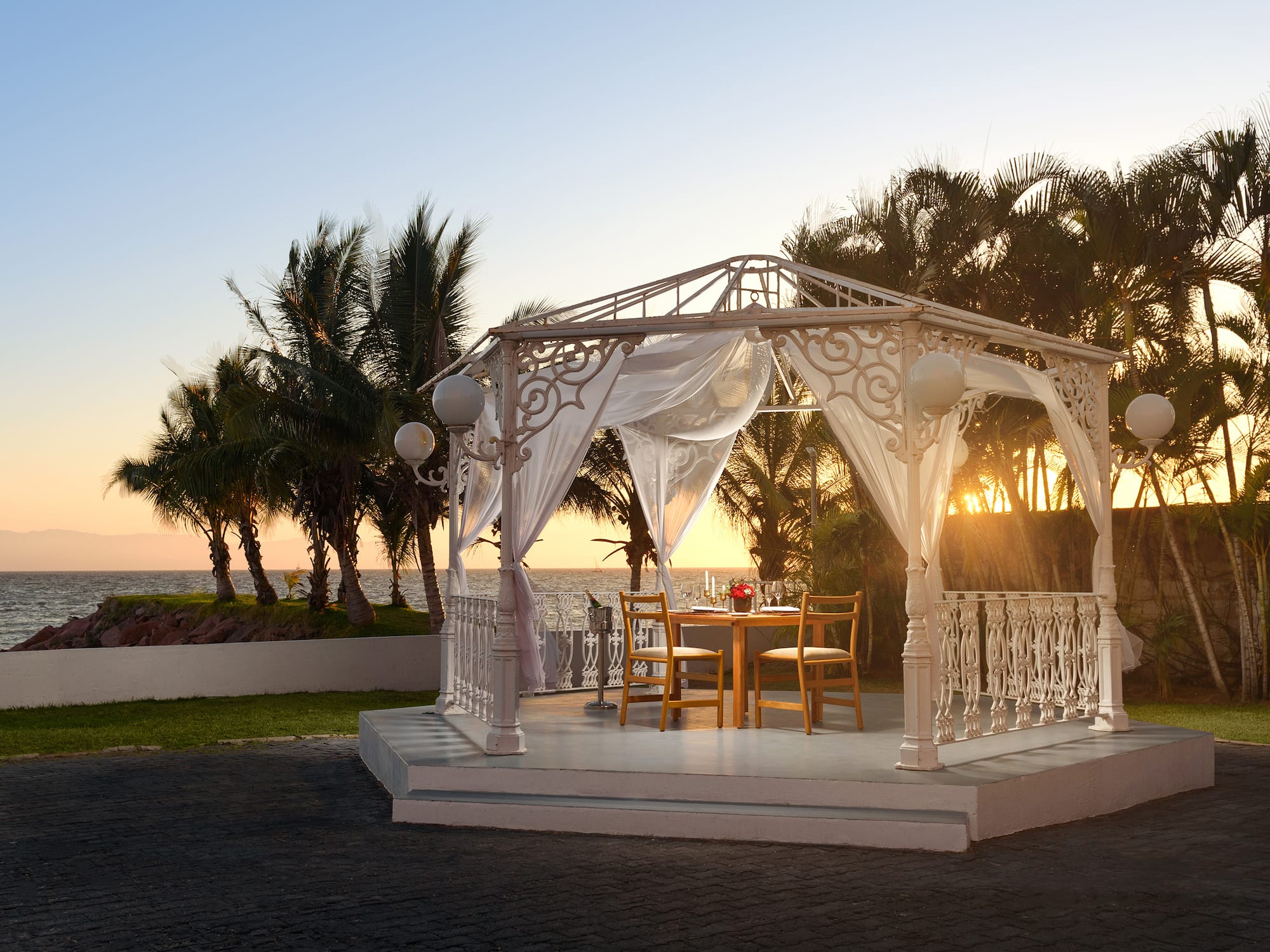 a white gazebo with a table and chairs on a patio with palm trees