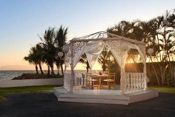 a white gazebo with a table and chairs on a patio with palm trees