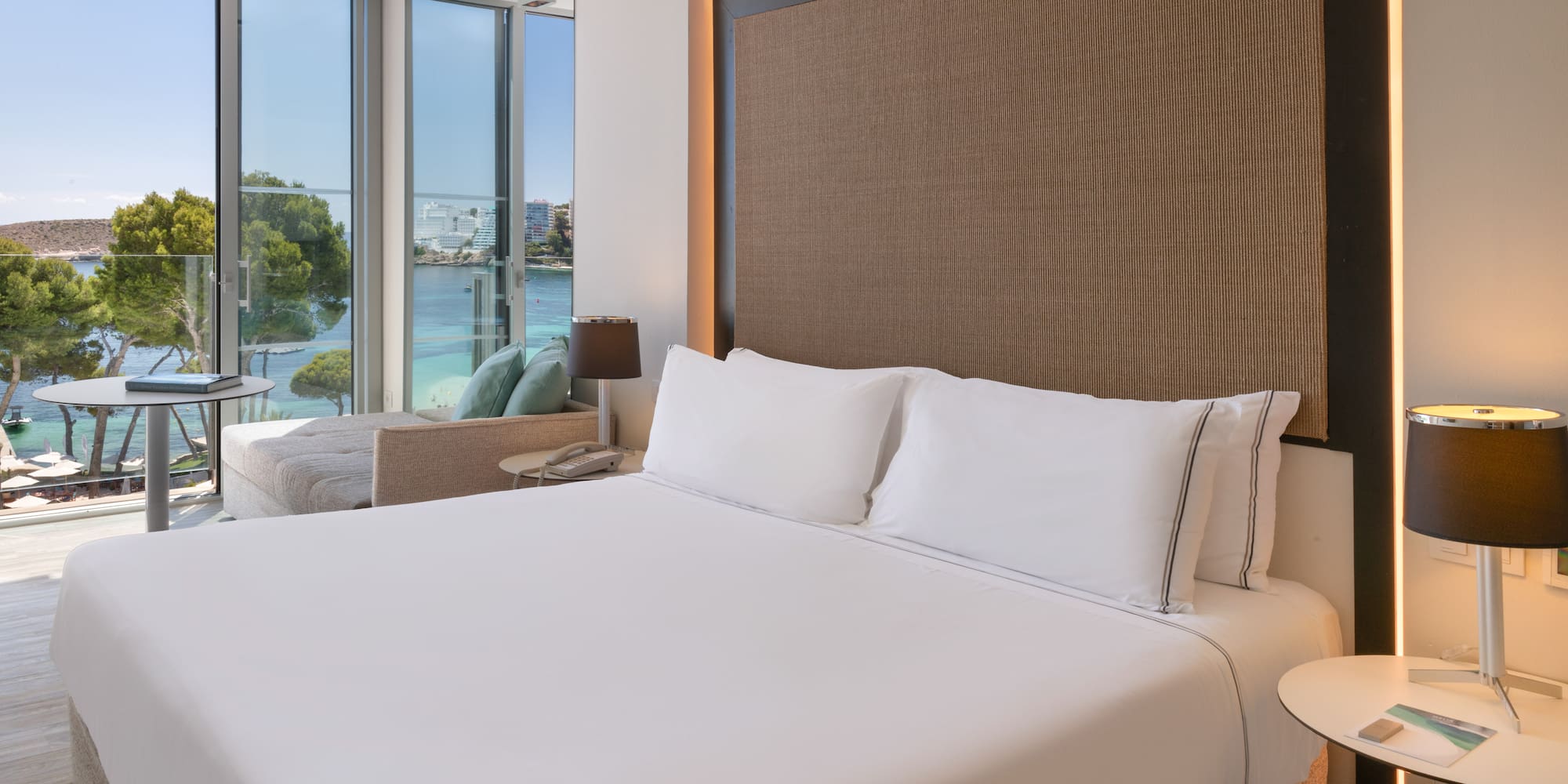 a bed with white sheets and a lamp next to a large window