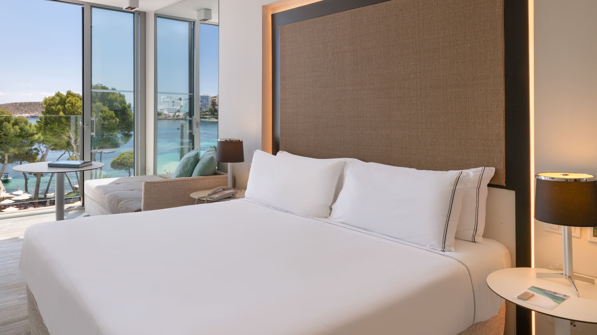 a bed with white sheets and a lamp next to a large window