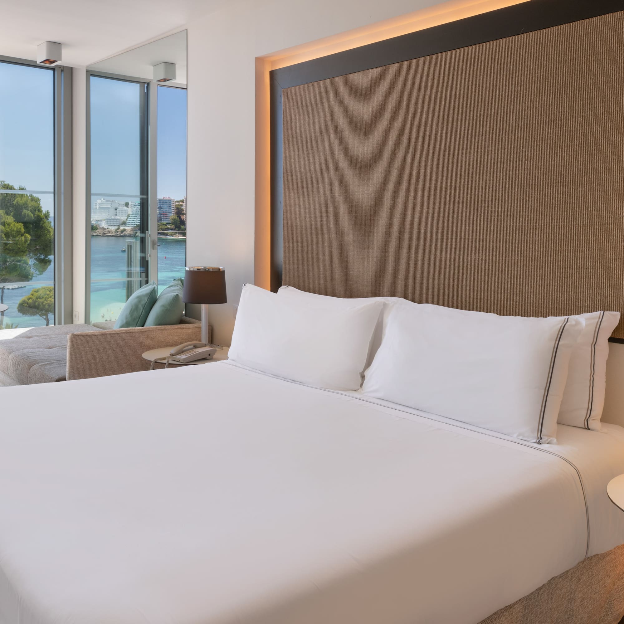 a bed with white sheets and a lamp next to a large window