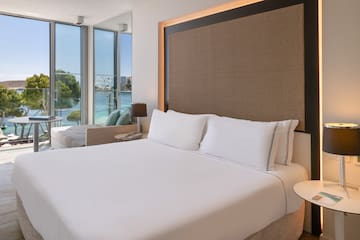 a bed with white sheets and a lamp next to a large window