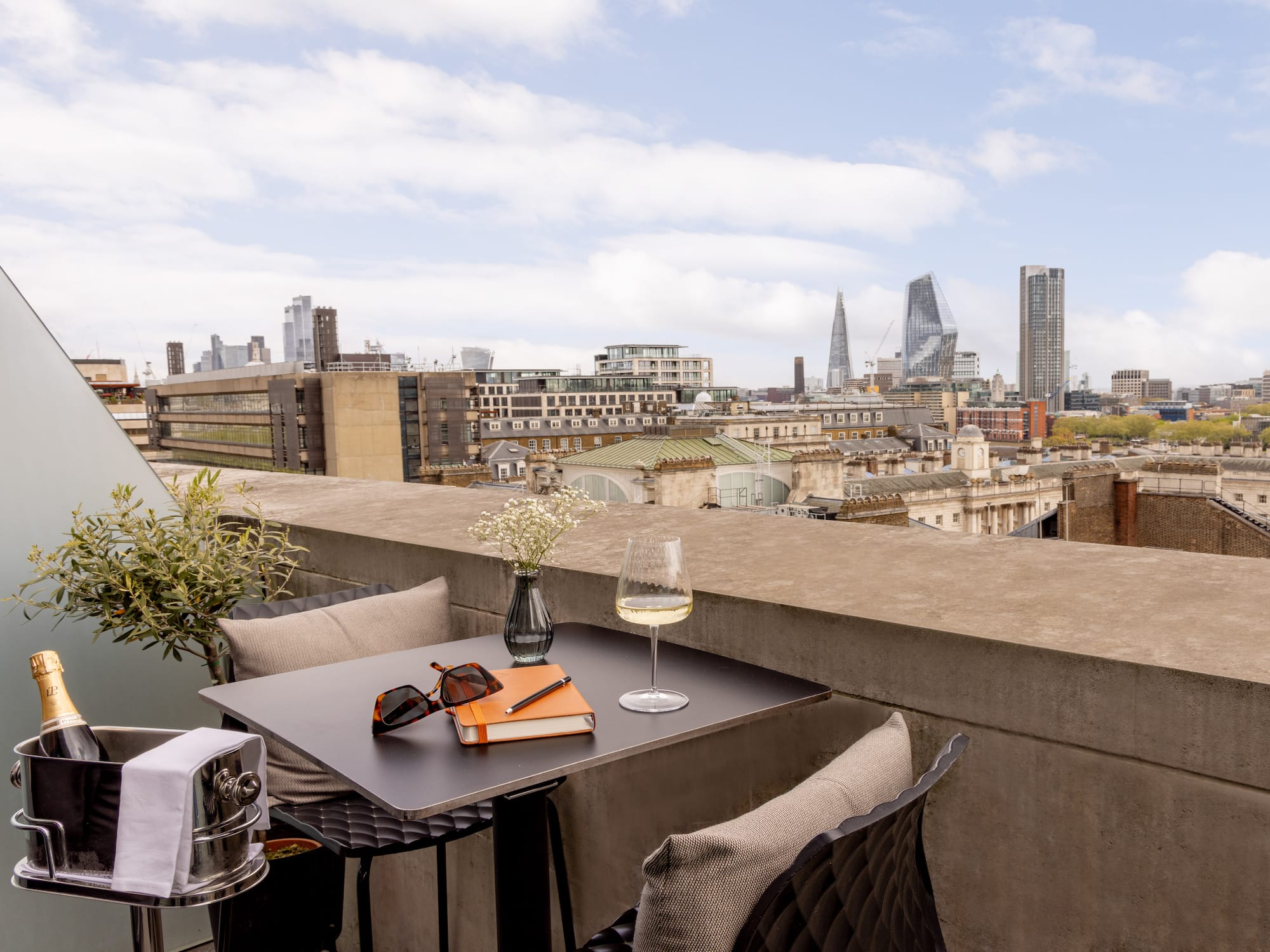 A table holds glasses and a book, with a city skyline in the background.