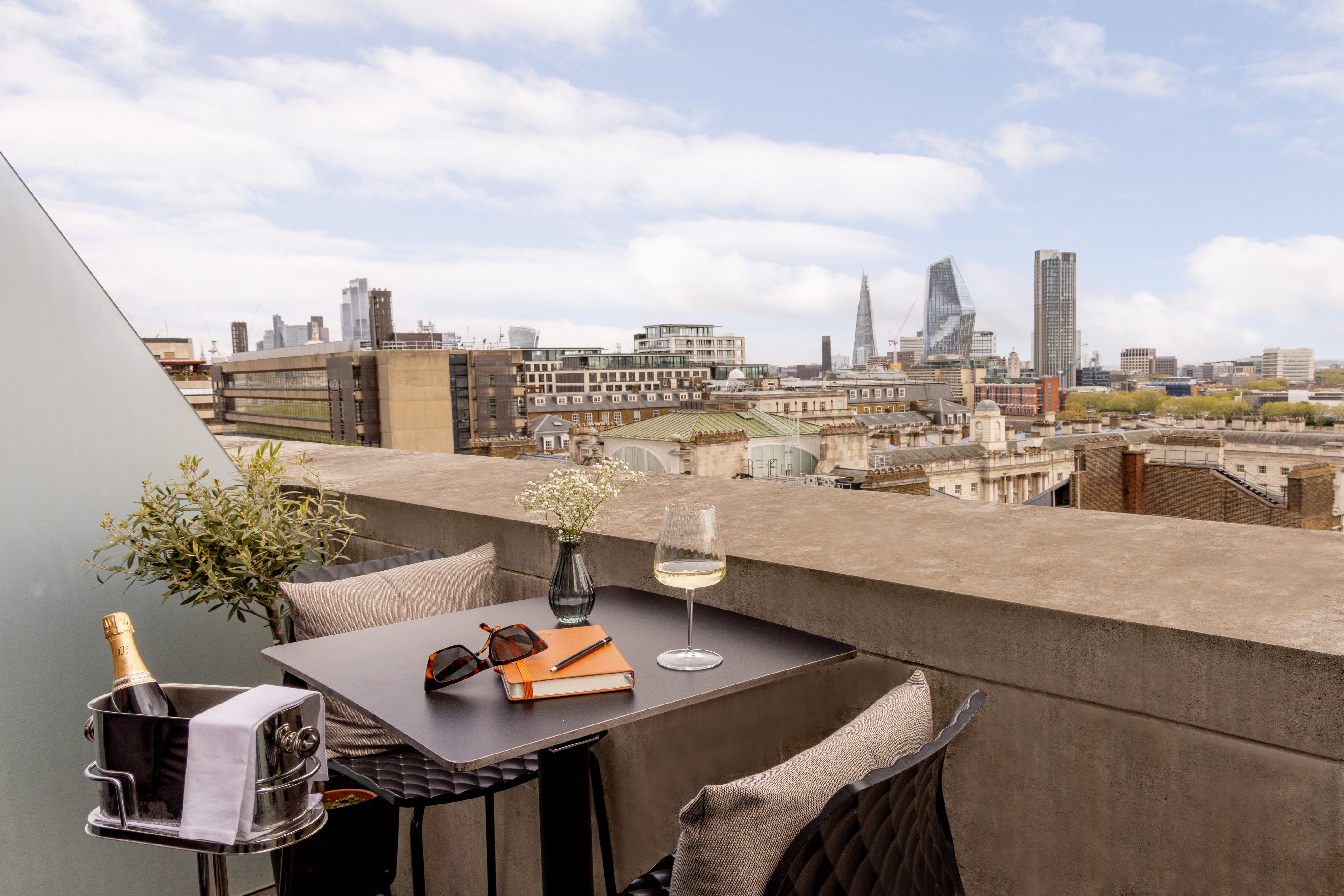 A table holds glasses and a book, with a city skyline in the background.