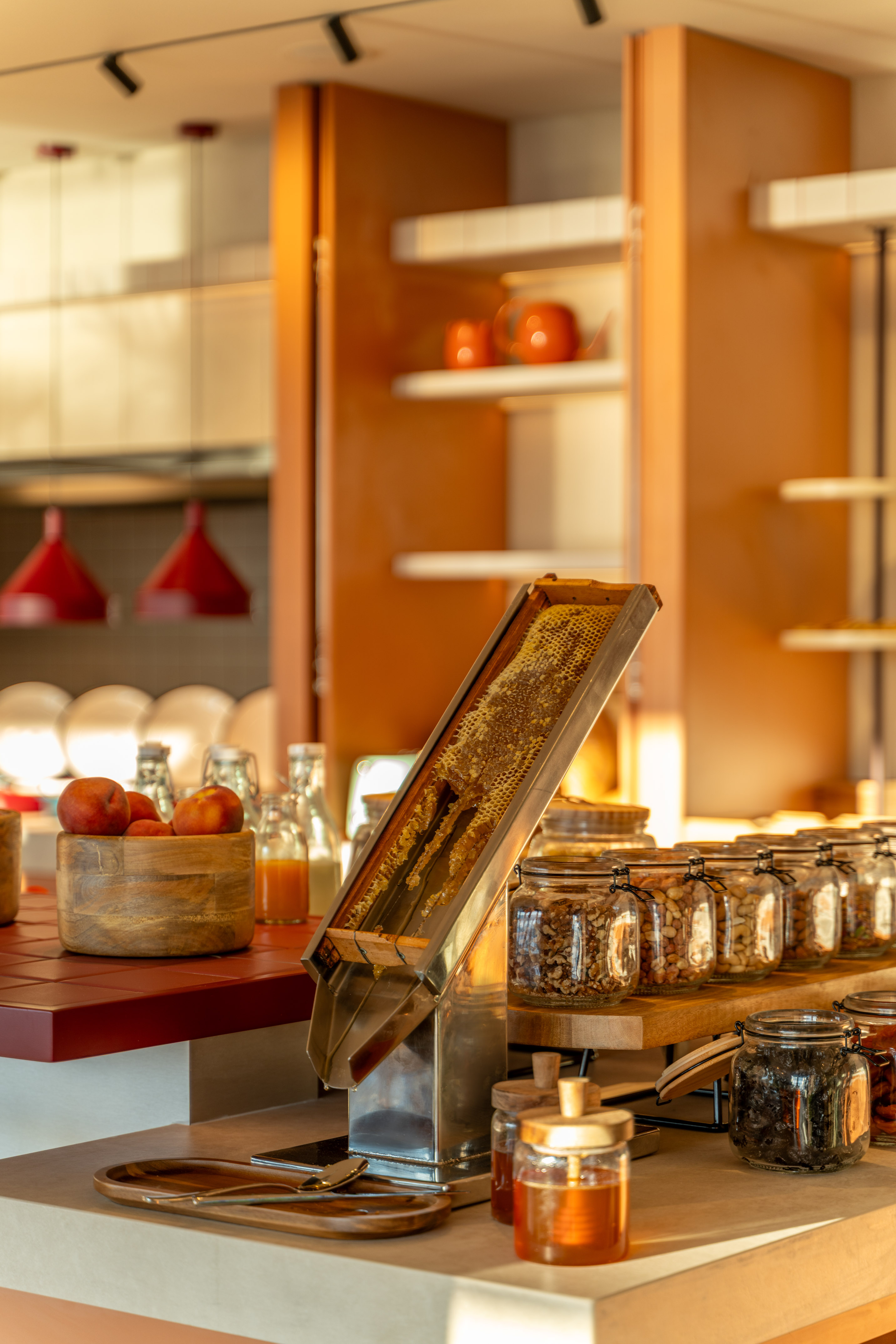 Honeycomb honey dispenser, nuts, and fruit on a breakfast buffet counter.