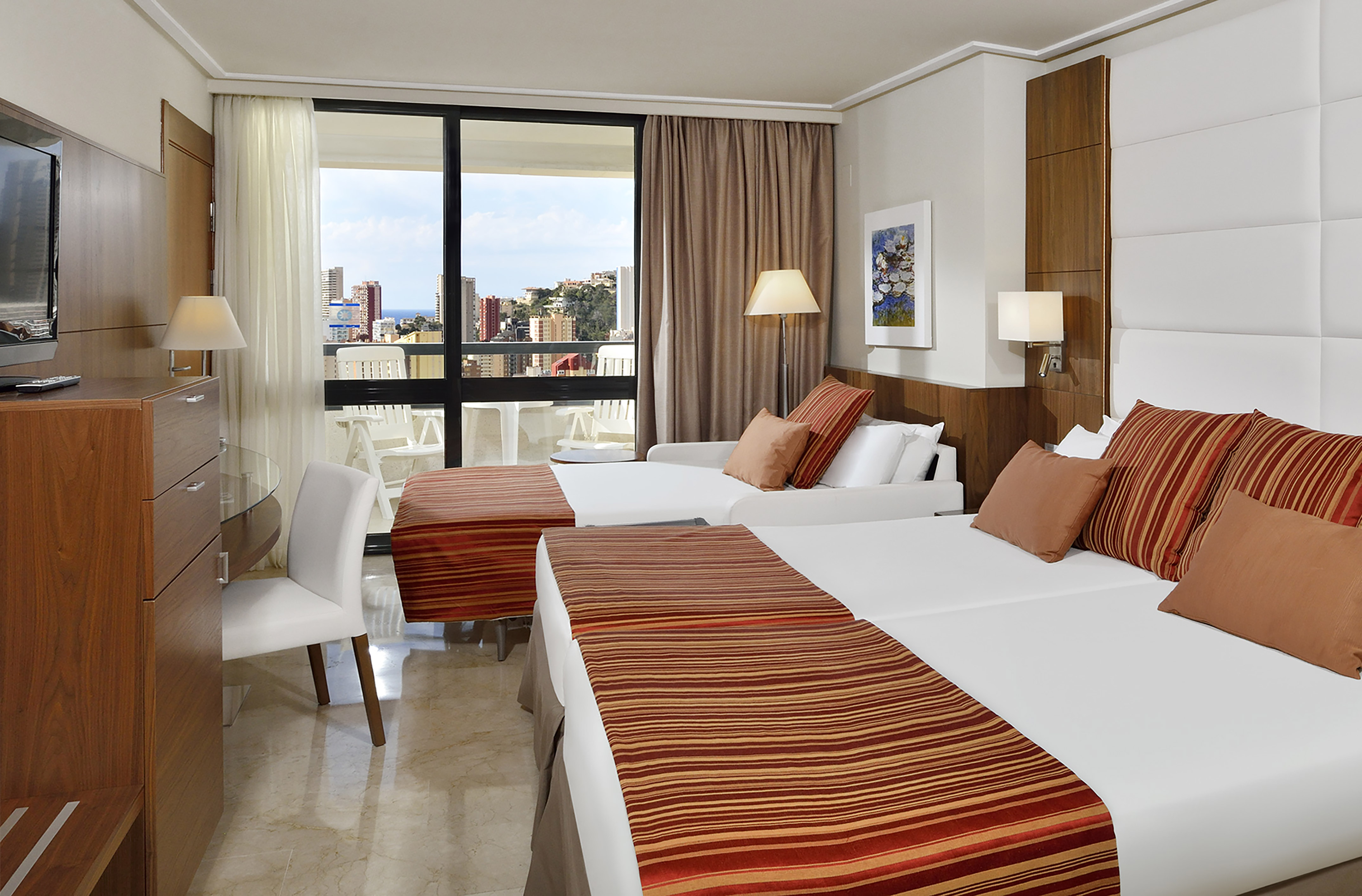 Twin bed hotel room with balcony overlooking city and ocean.