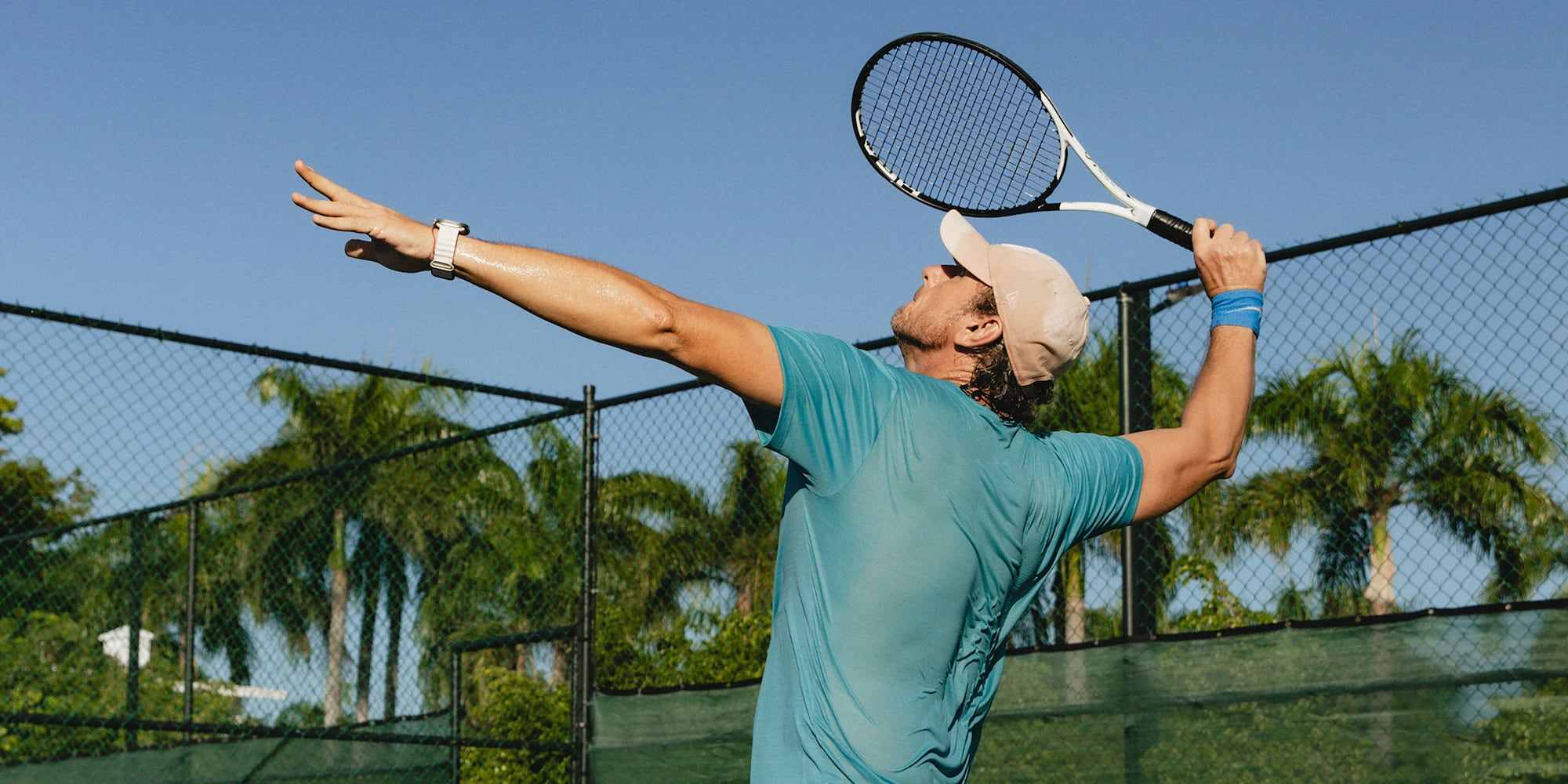 Male tennis player executing an overhead serve on an outdoor court.