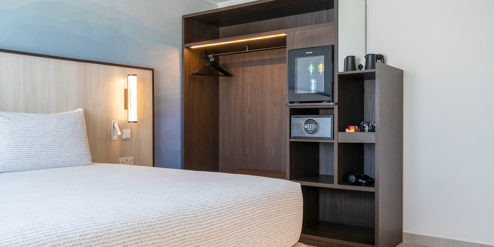 Modern hotel bedroom with built-in wardrobe, minibar, safe, and patterned bed. - The INNSiDE Room - INNSiDE Bugibba, بوجيبا