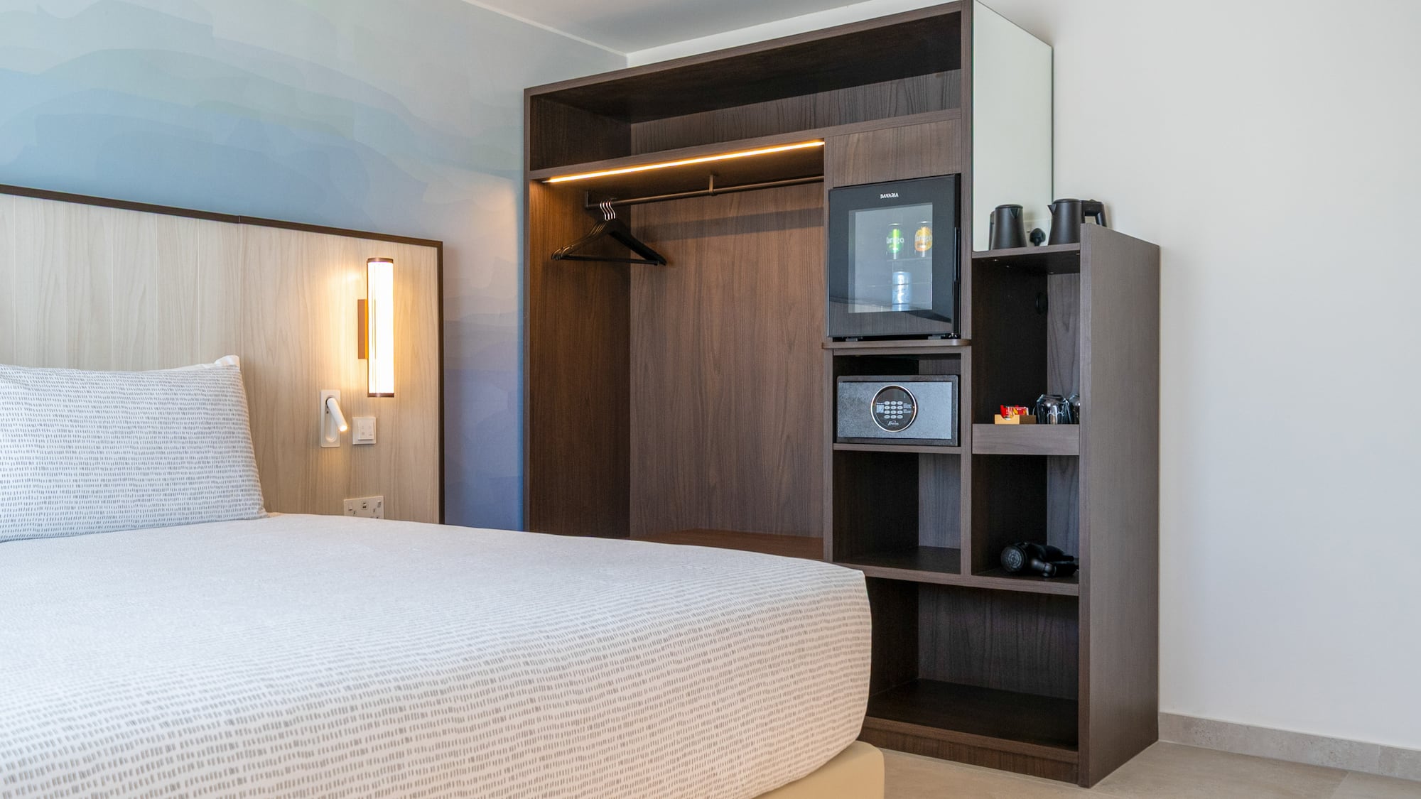 Modern hotel bedroom with built-in wardrobe, minibar, safe, and patterned bed. - The INNSiDE Room - INNSiDE Bugibba, ブジッバ