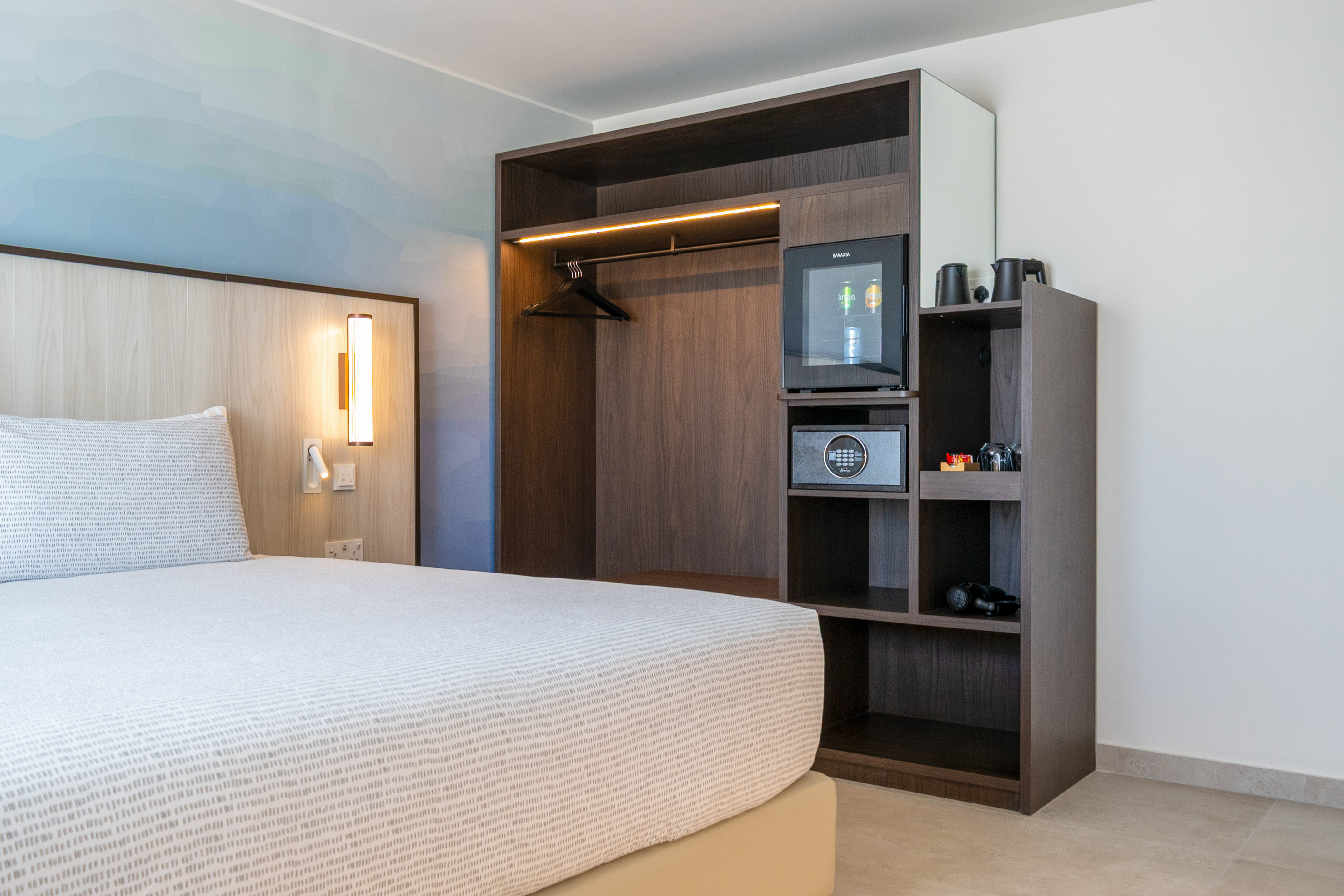 Modern hotel bedroom with built-in wardrobe, minibar, safe, and patterned bed. - The INNSiDE Room - INNSiDE Bugibba, ブジッバ