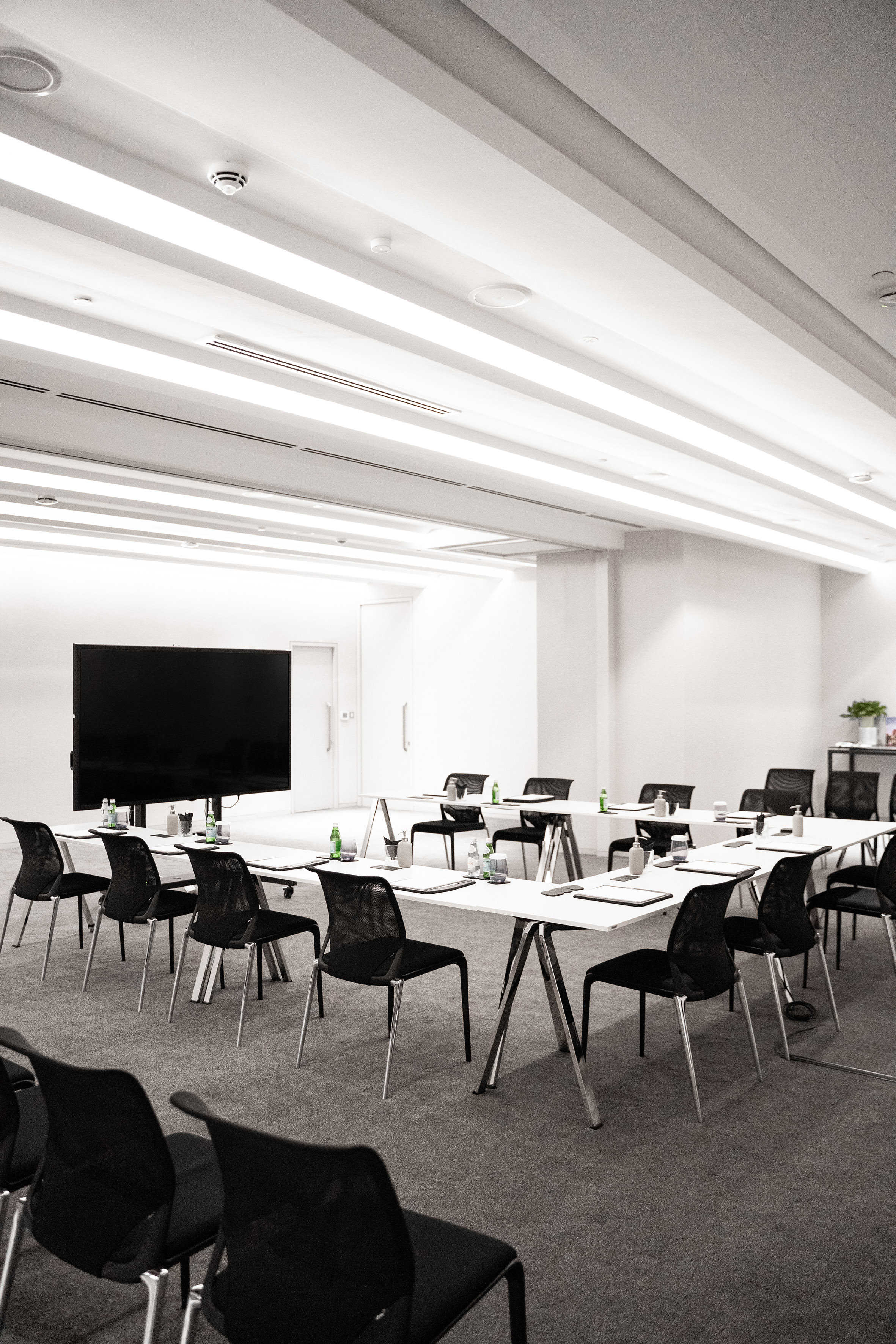 Empty modern conference room with U-shaped tables, black chairs, and large display.