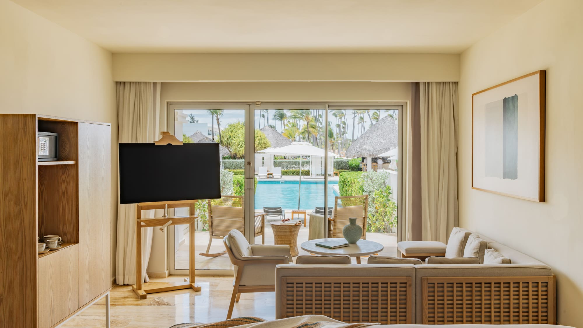 Modern resort suite with living area, TV, and pool view with tropical garden.