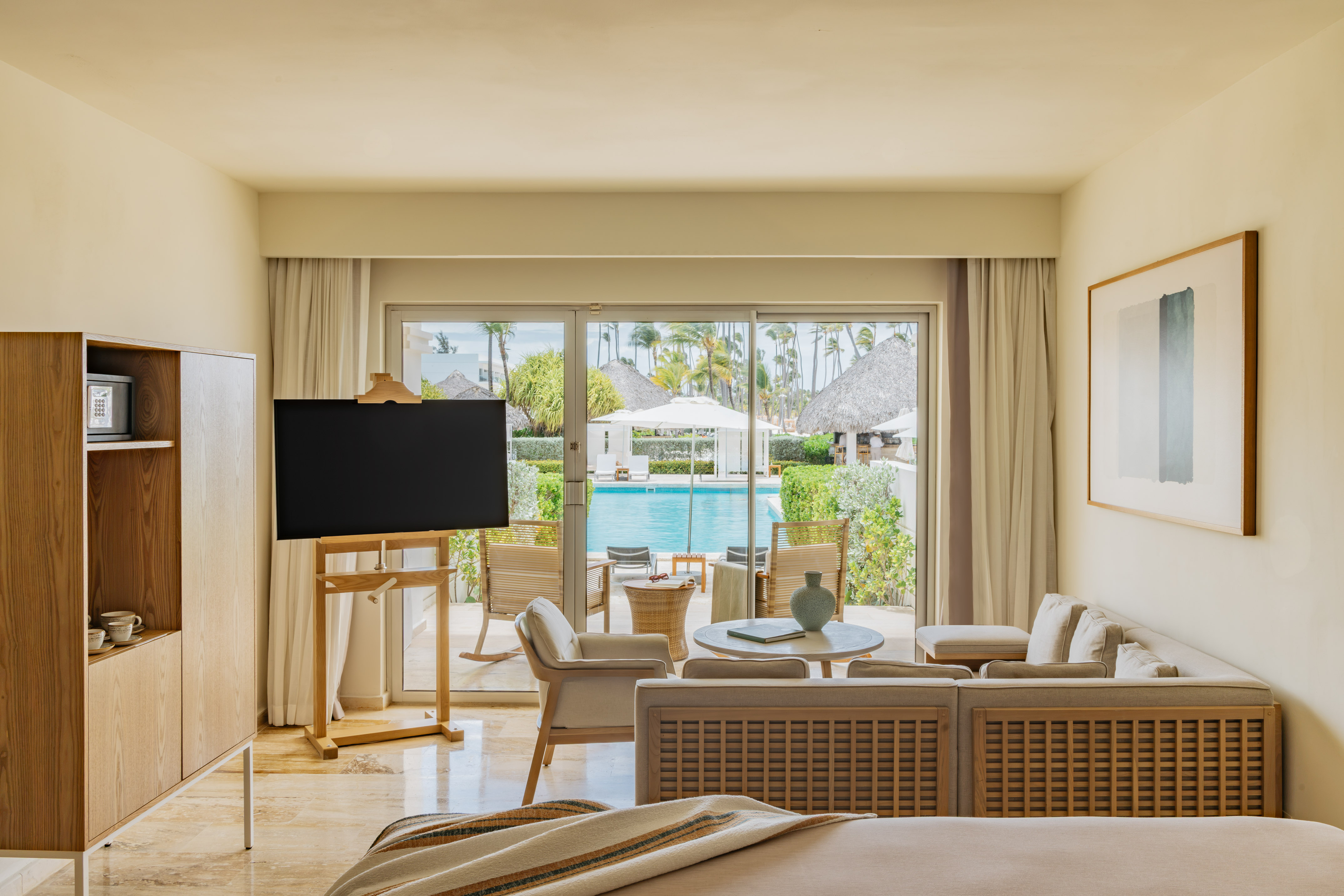Modern resort suite with living area, TV, and pool view with tropical garden.
