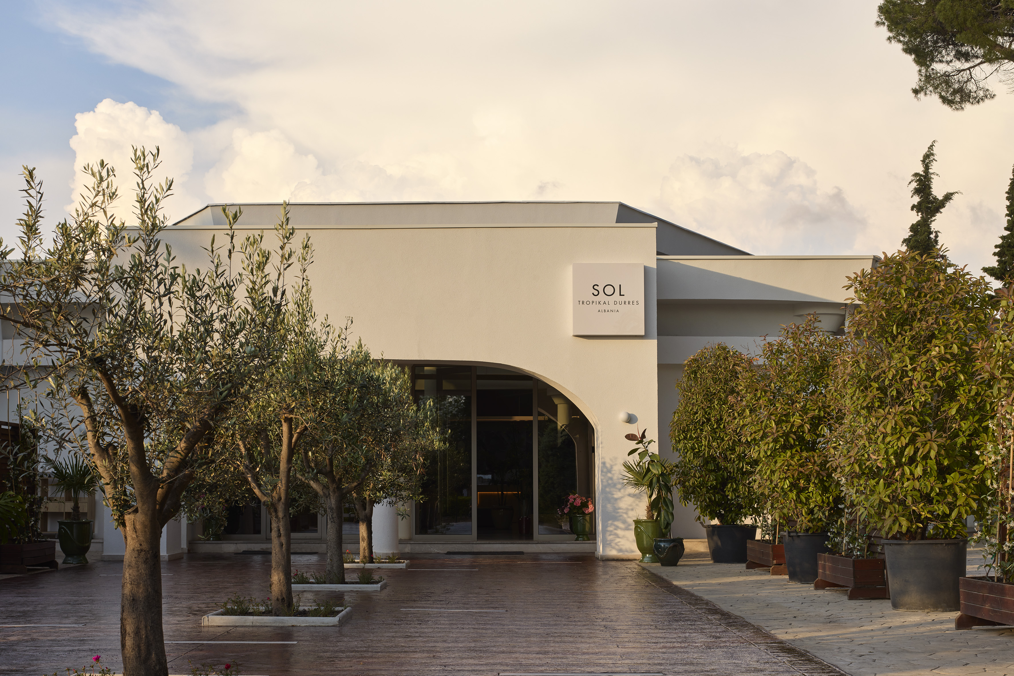 Sol Tropical Durres, Albania hotel entrance with modern building and olive trees.