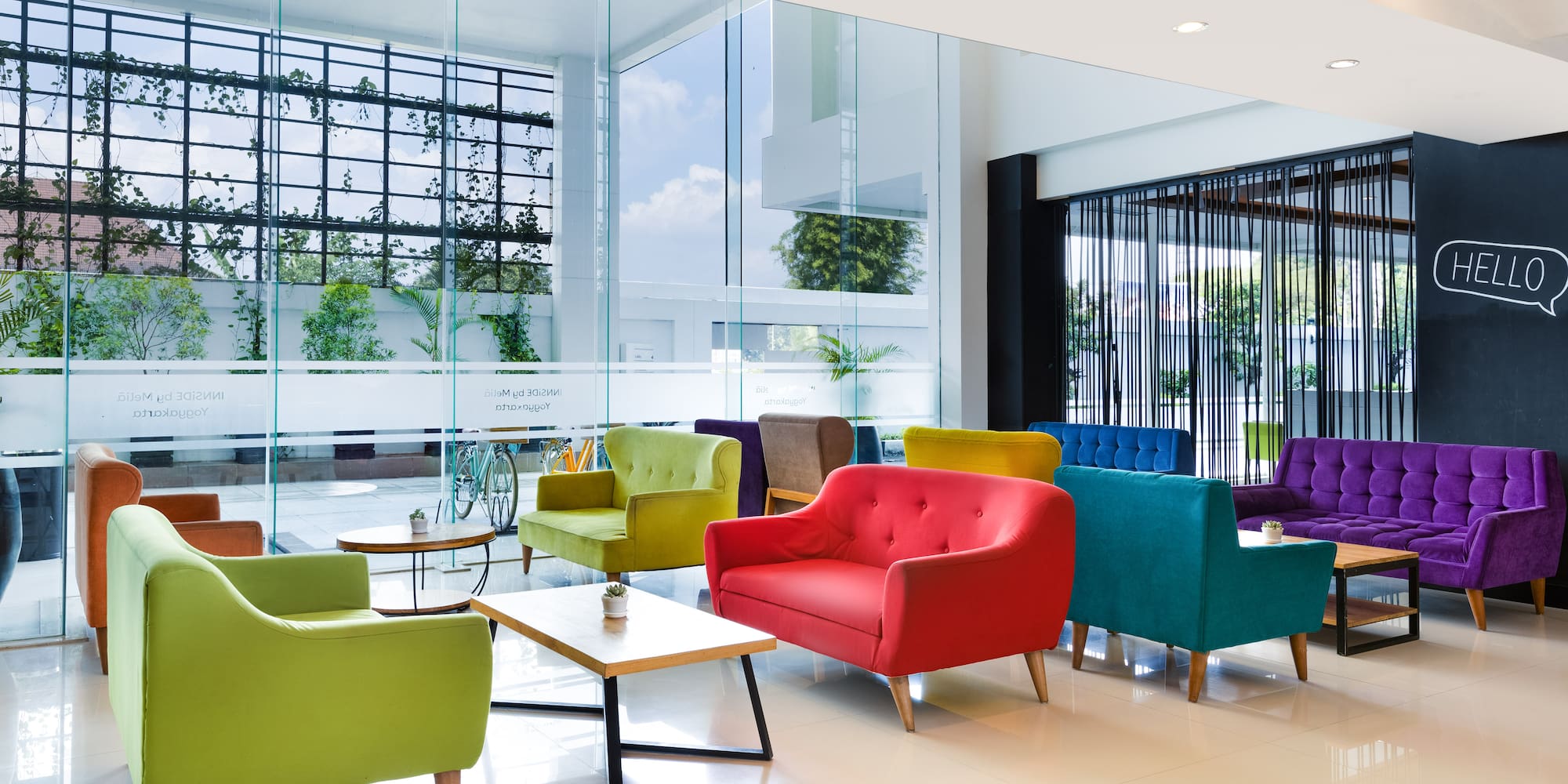Modern lobby with vibrant lounge chairs, glass walls, and sunlight.