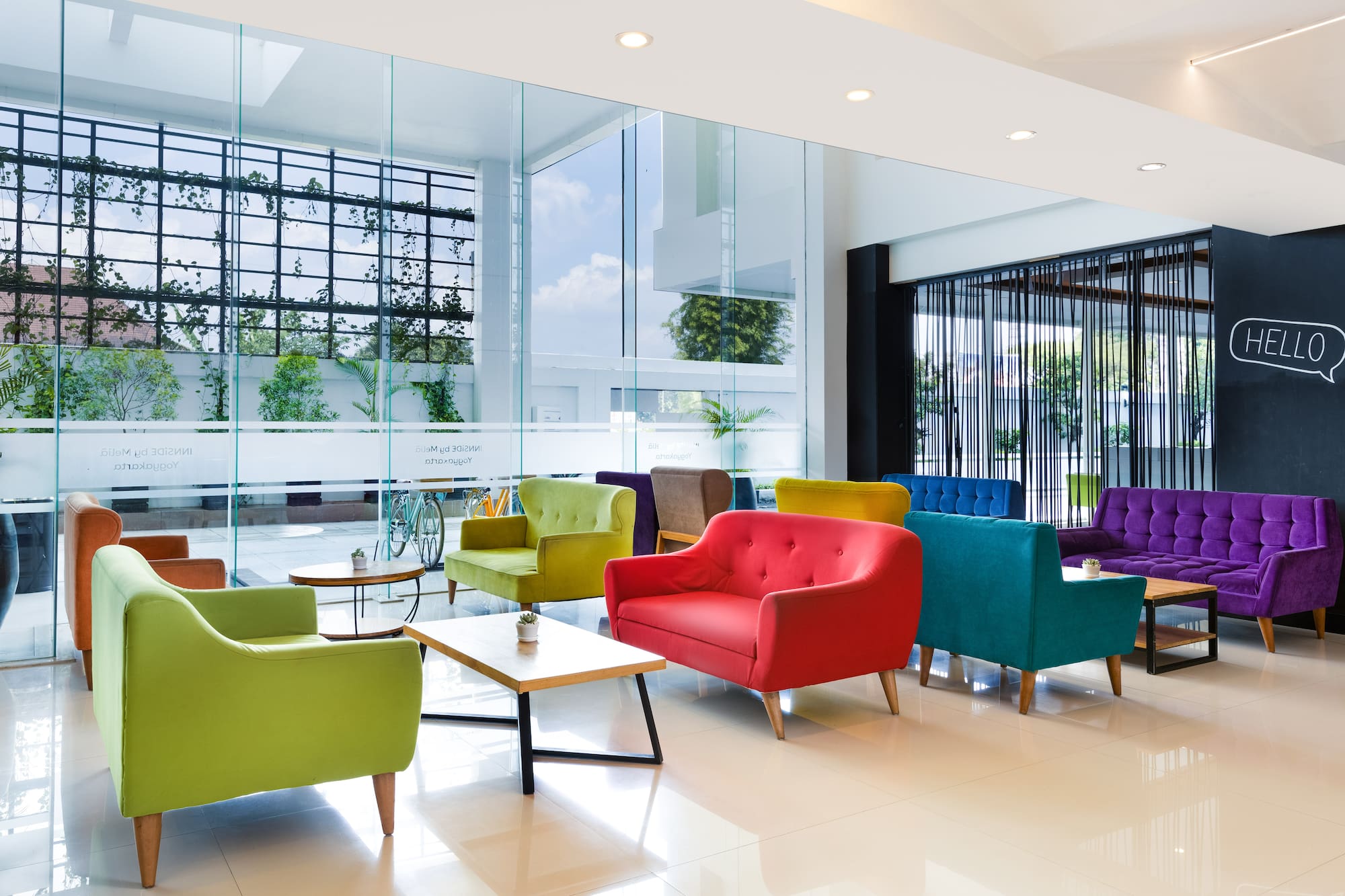 Modern lobby with vibrant lounge chairs, glass walls, and sunlight.