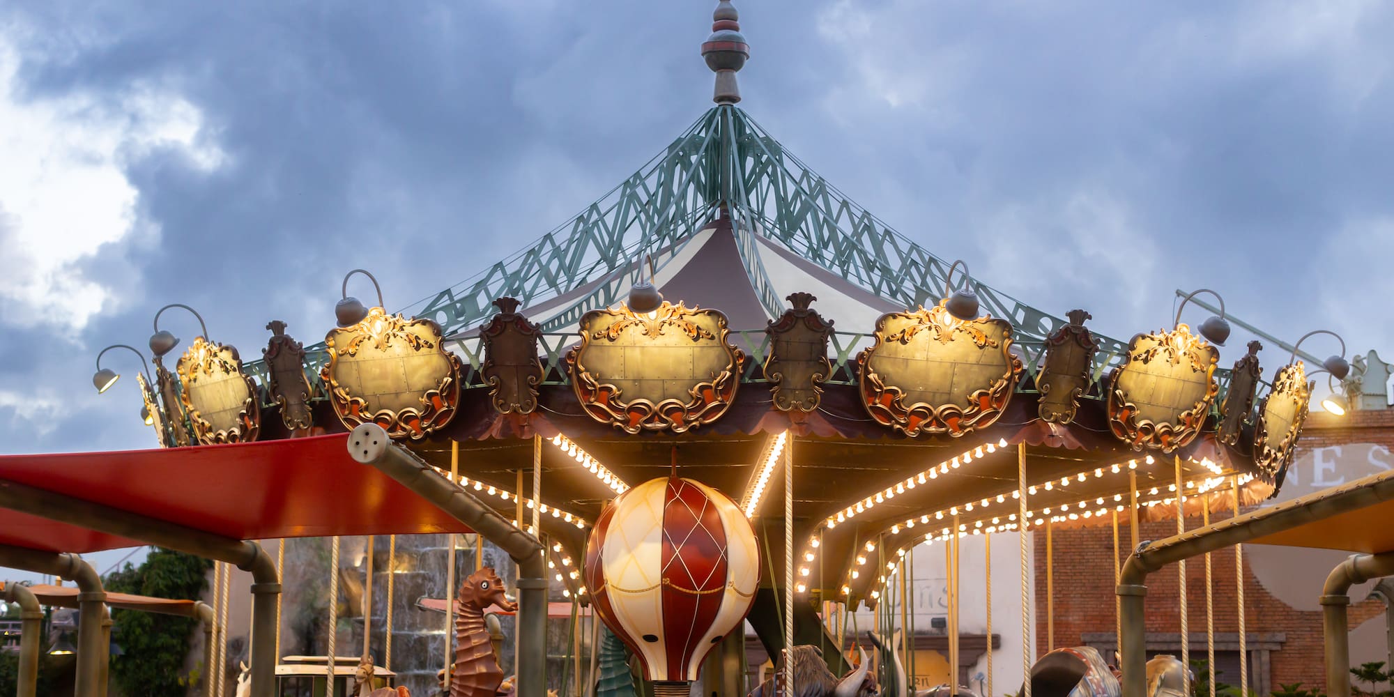 Ornate carousel with glowing lights, seahorse, and bull figures under evening sky.