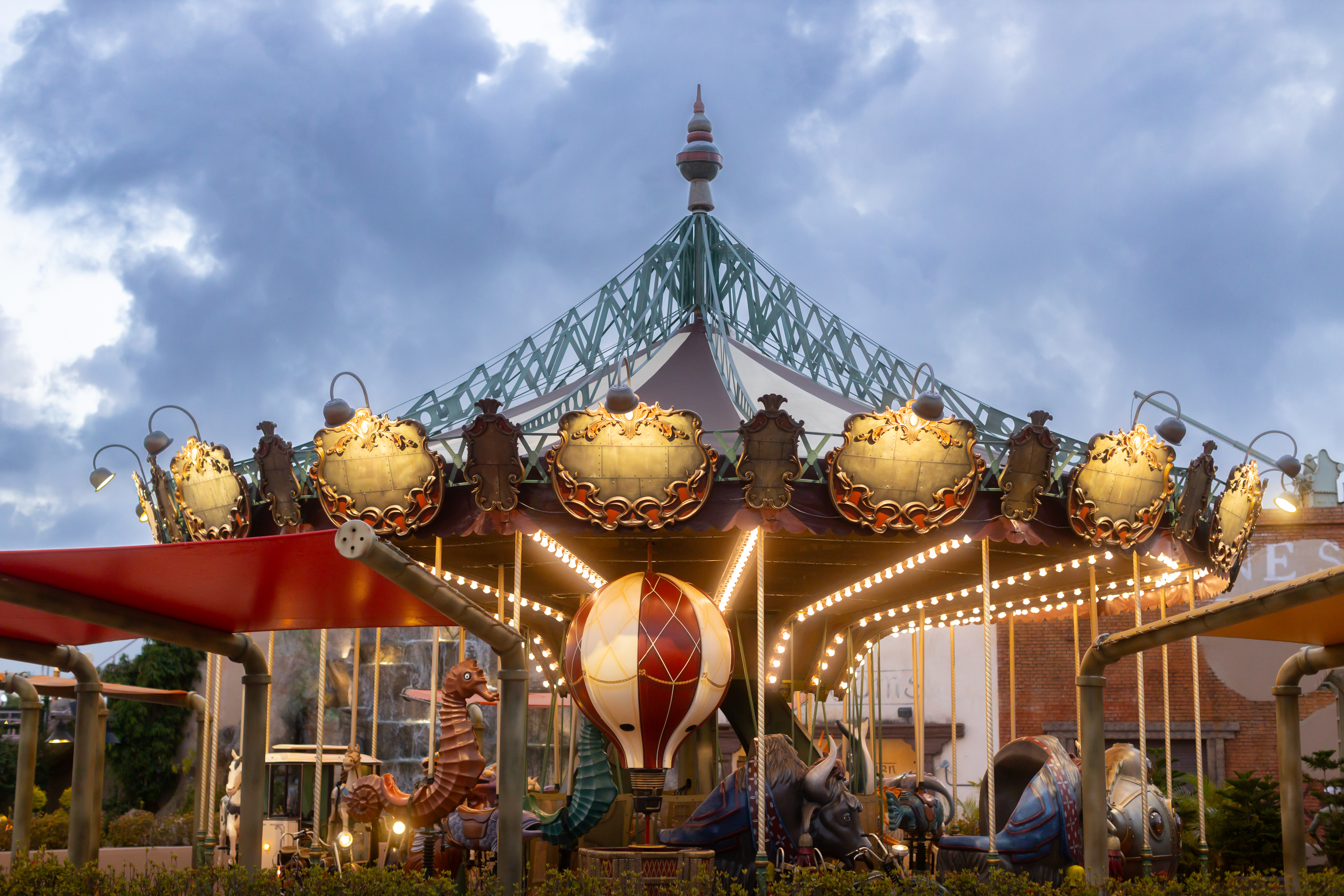 Ornate carousel with glowing lights, seahorse, and bull figures under evening sky.