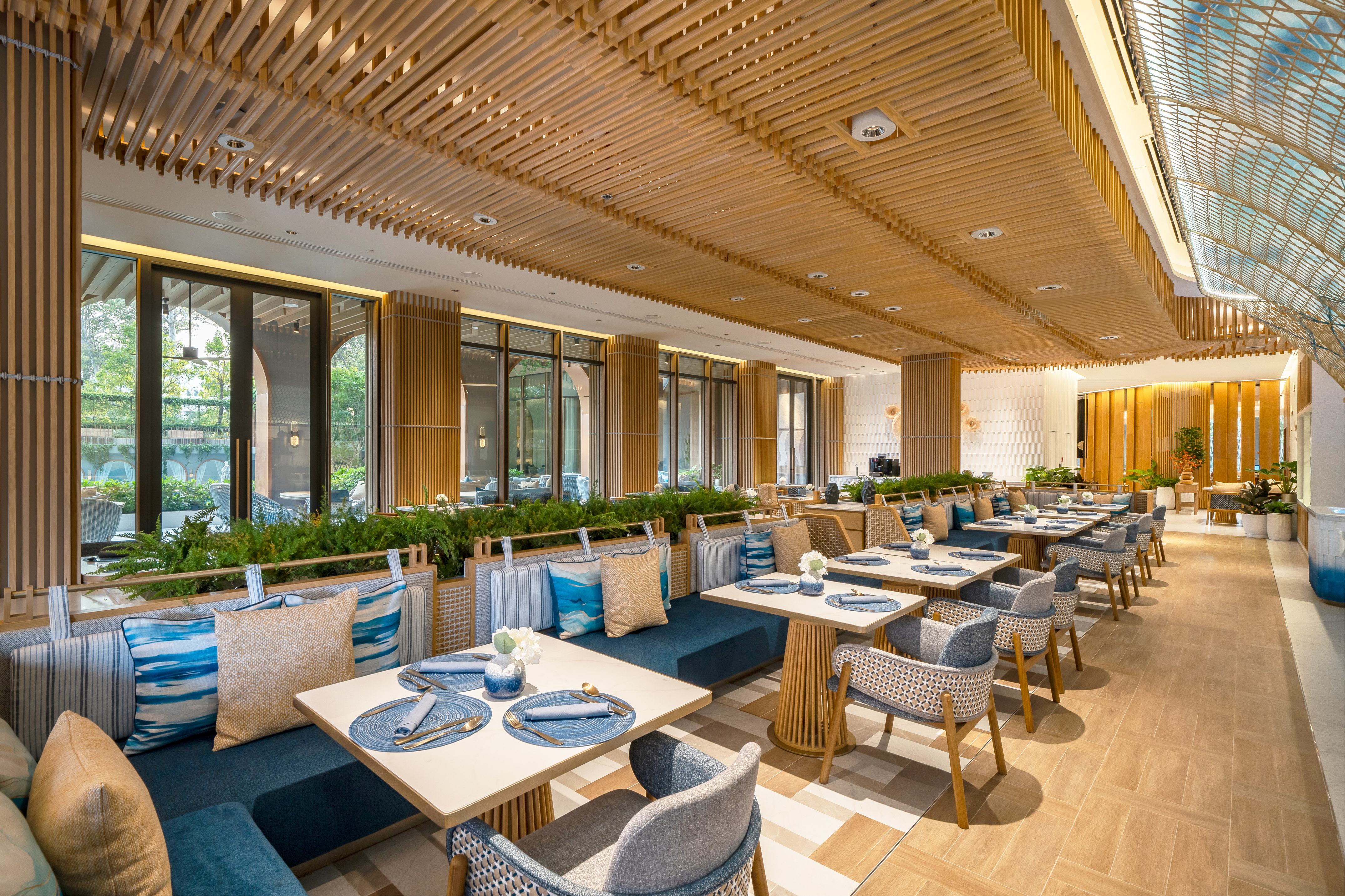 Modern restaurant interior, wooden ceiling, blue seating, large windows overlooking greenery.