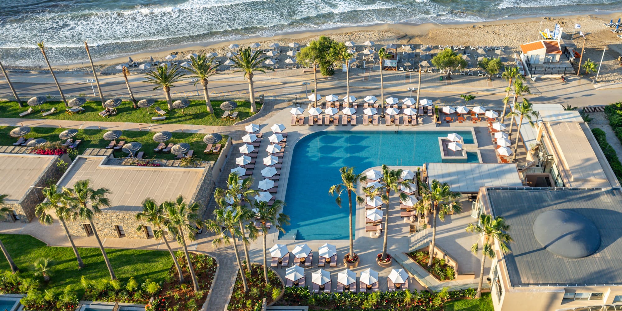 Aerial view: luxury beachfront resort with pools, palm trees, sandy beach, ocean.