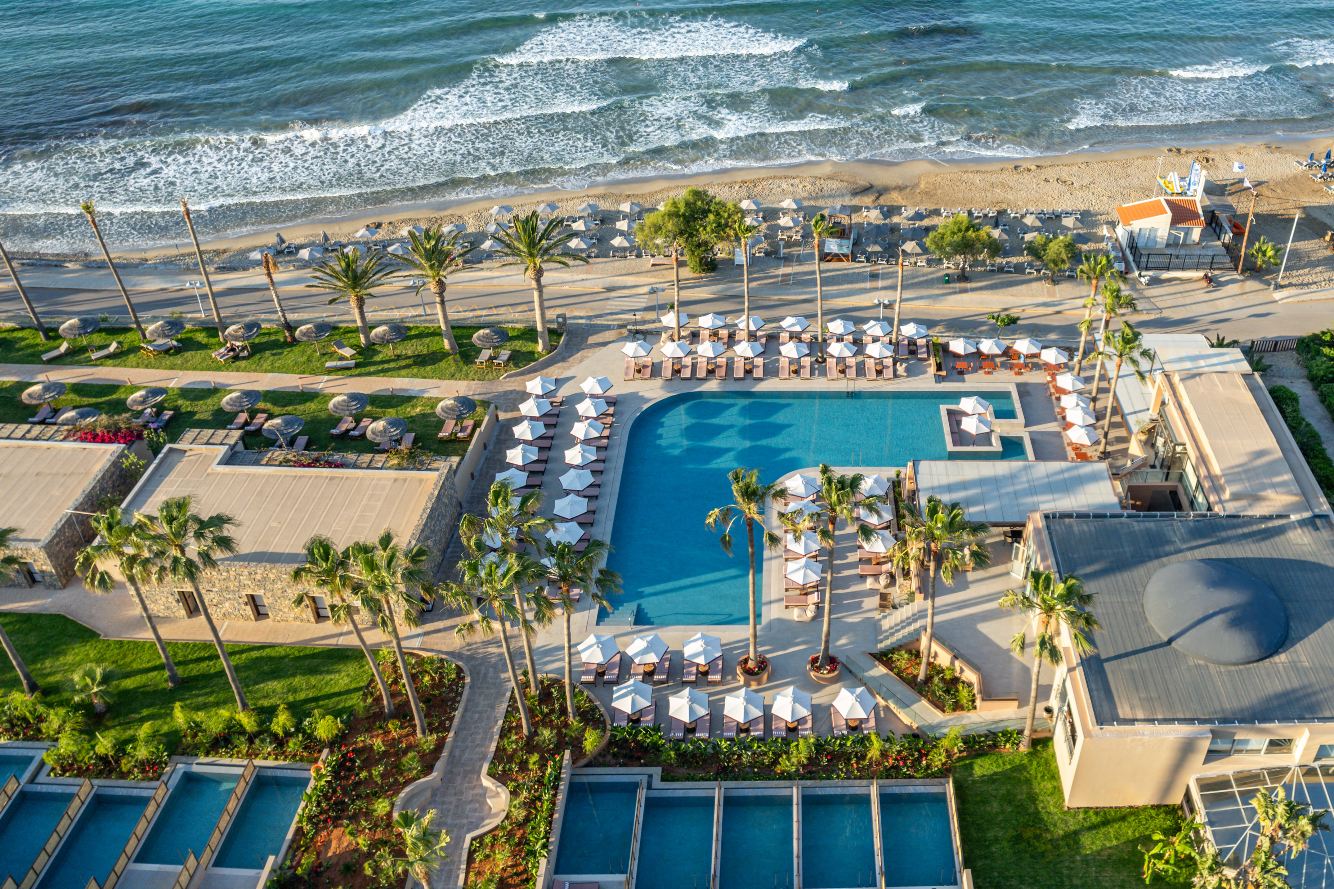 Aerial view: luxury beachfront resort with pools, palm trees, sandy beach, ocean.