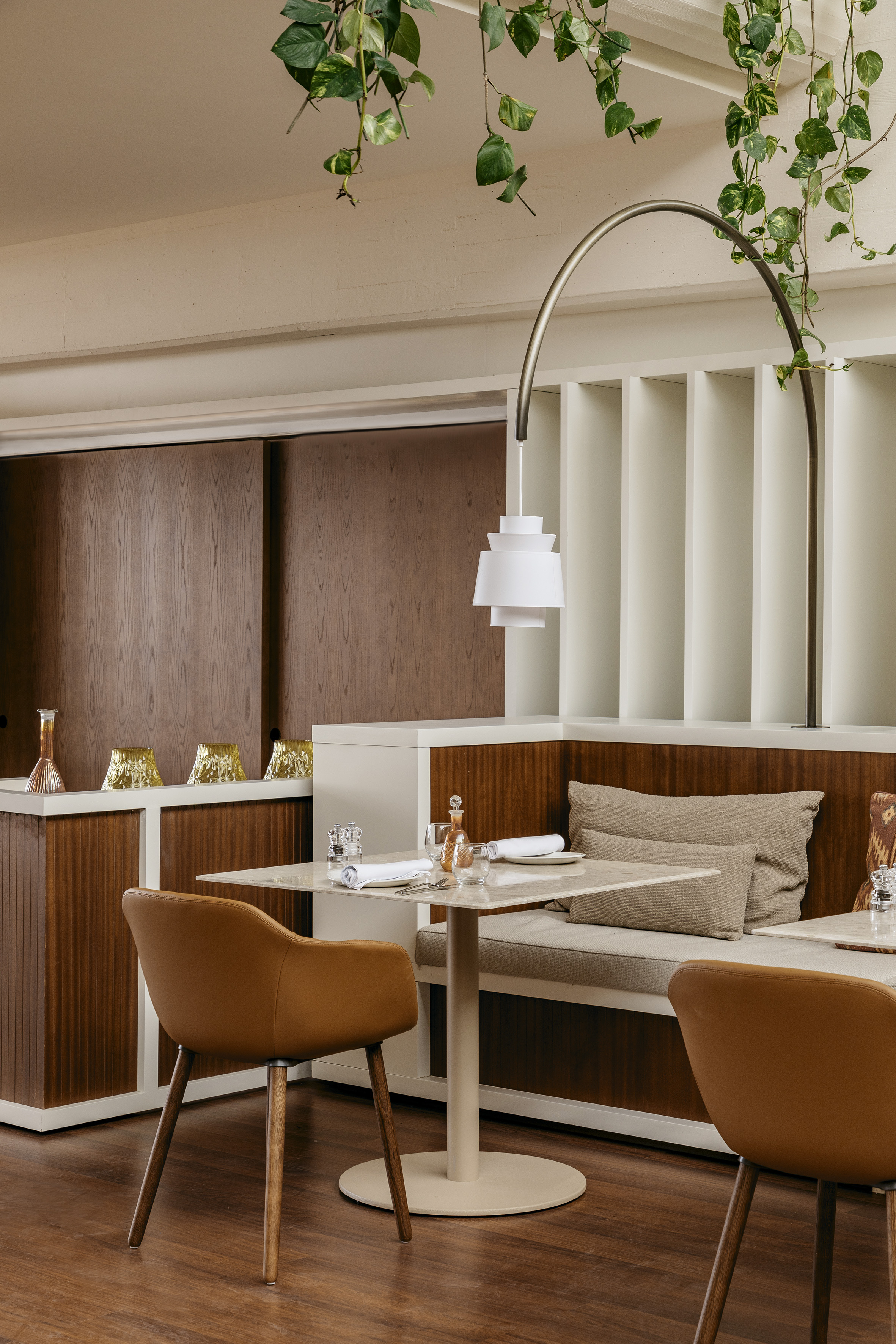 Modern restaurant interior with wood, banquette, tan chairs, set table, plants.