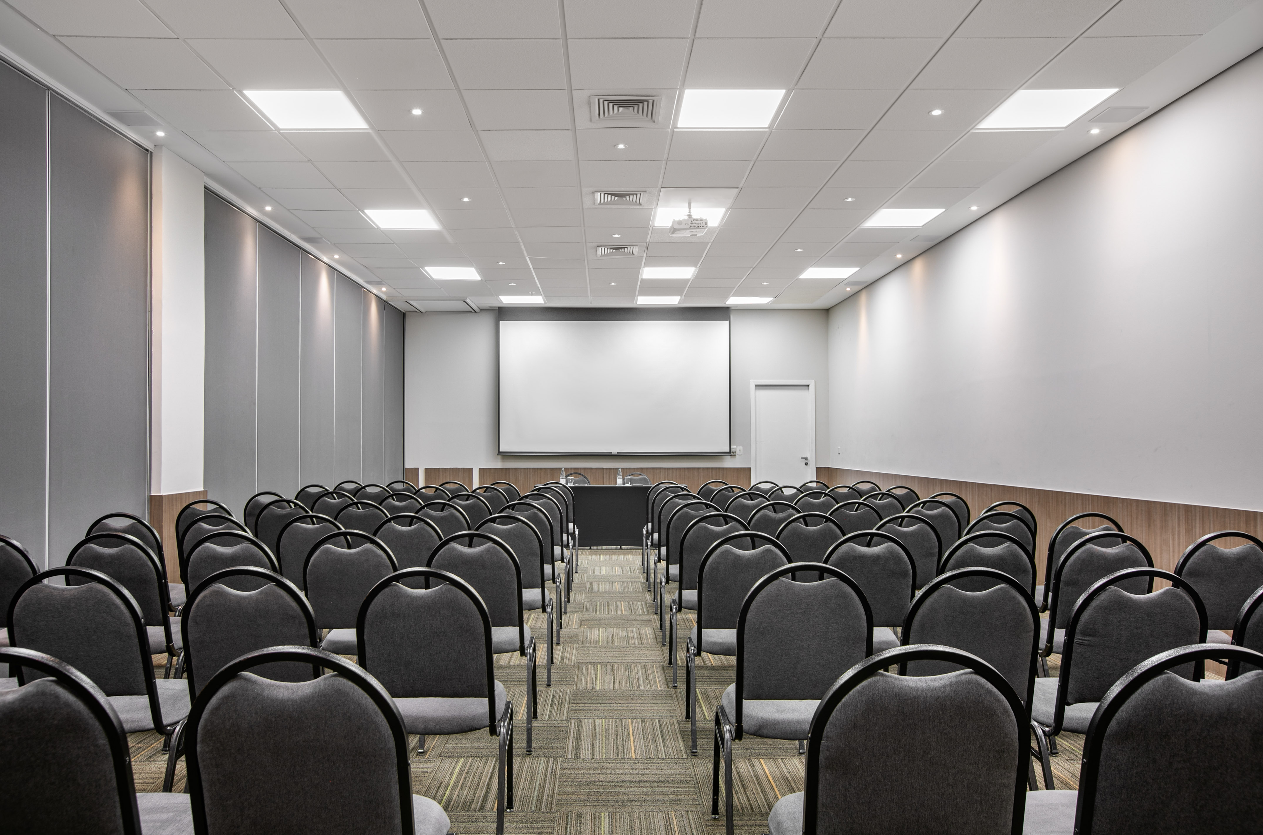 Empty conference room with rows of grey chairs, projector, and blank screen.