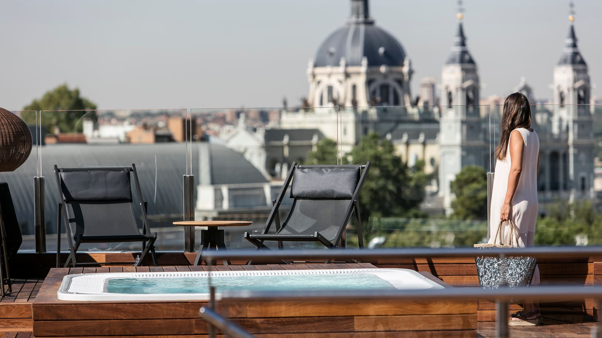 A woman stands on a deck beside a hot tub, with a city skyline visible in the background.