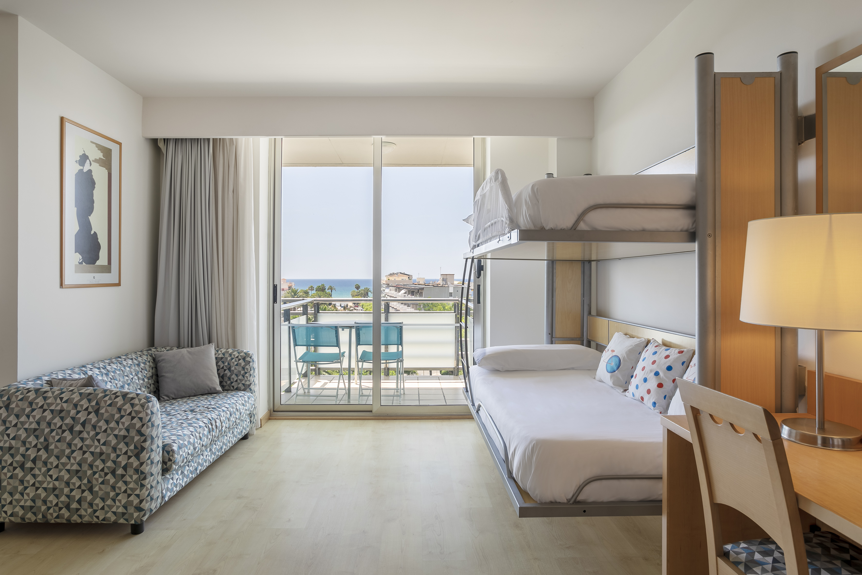 Family hotel room with bunk beds, sofa, desk, and sea view balcony.