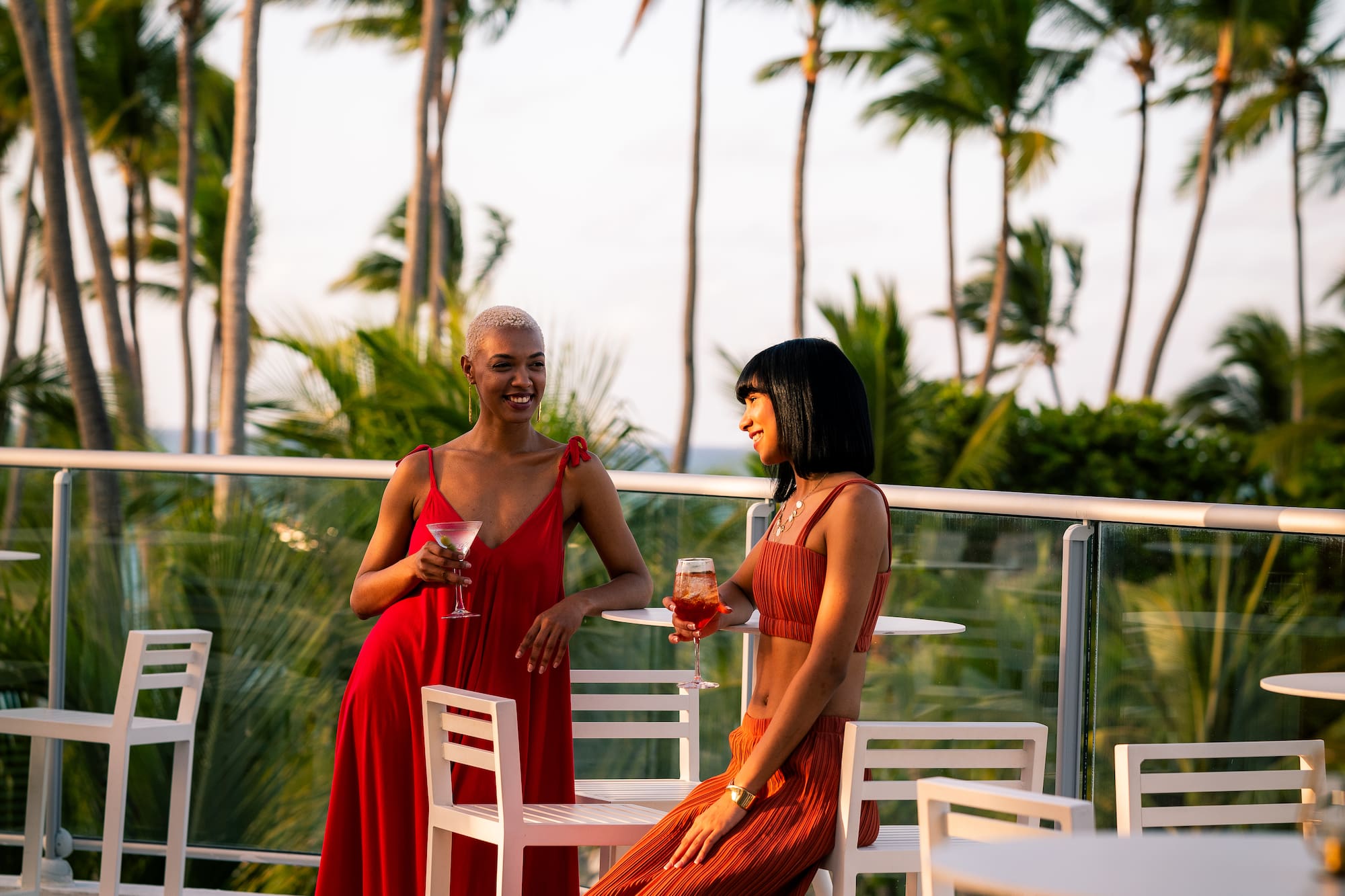 two women in red dresses sitting at a table with drinks