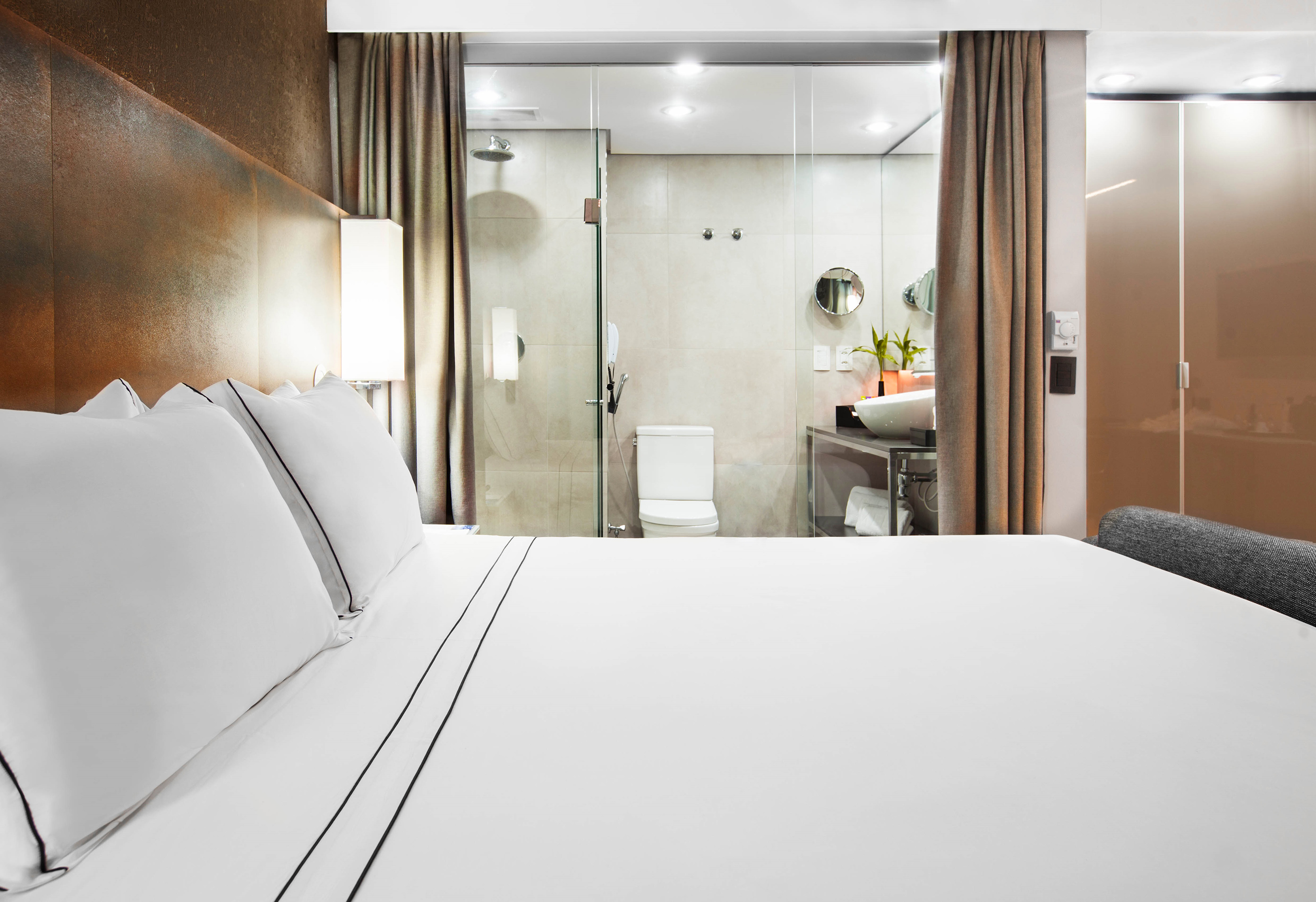 Modern hotel room with white bed, textured headboard, and open ensuite bathroom.