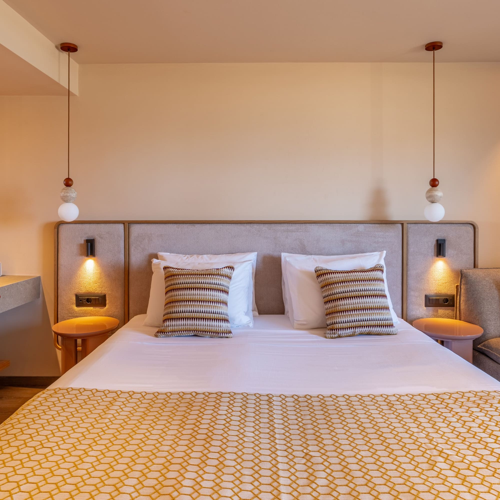 Modern hotel bedroom with large bed, geometric throw, red sink, and lounge.