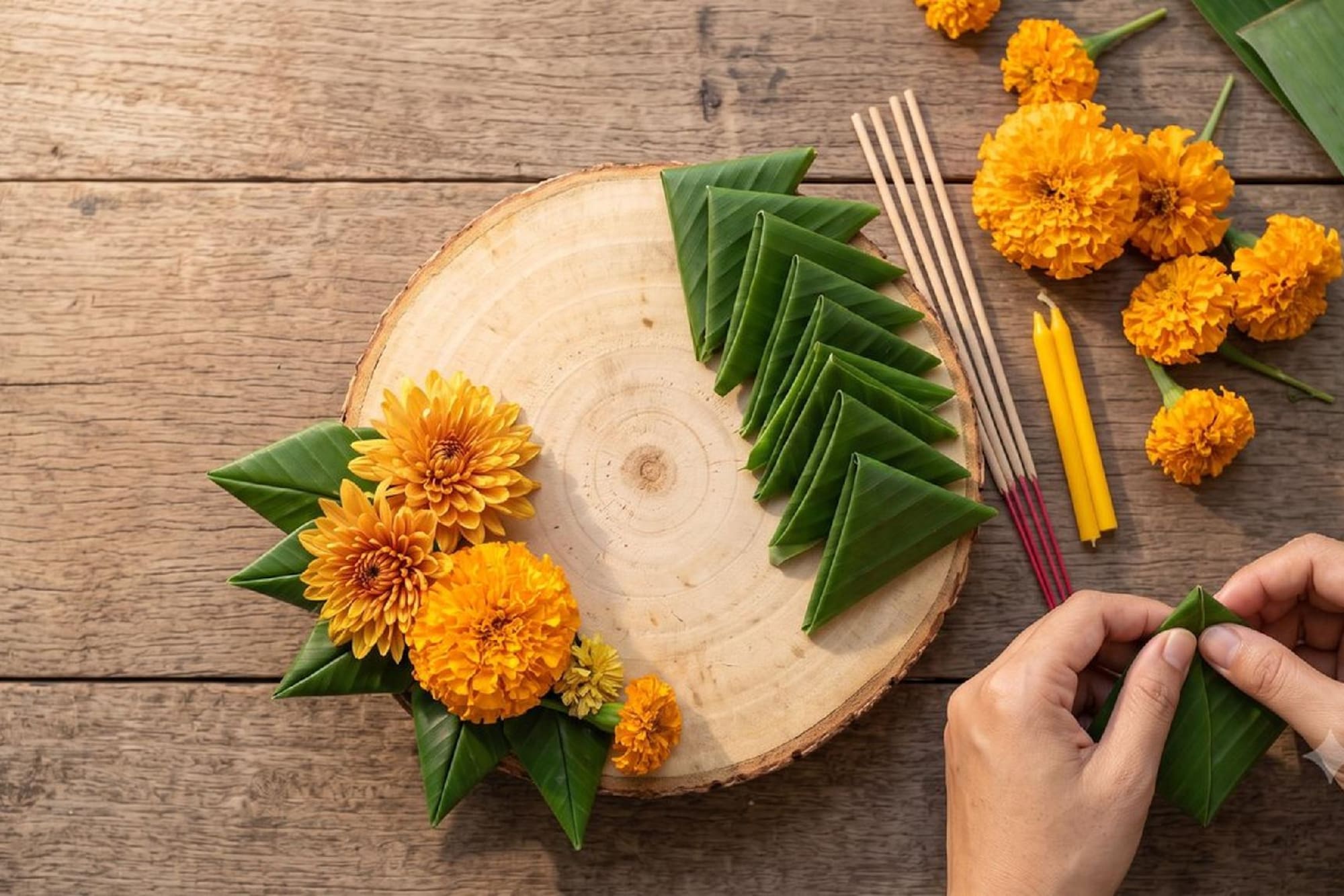 Crafting traditional offering: folded banana leaves, orange flowers, incense.