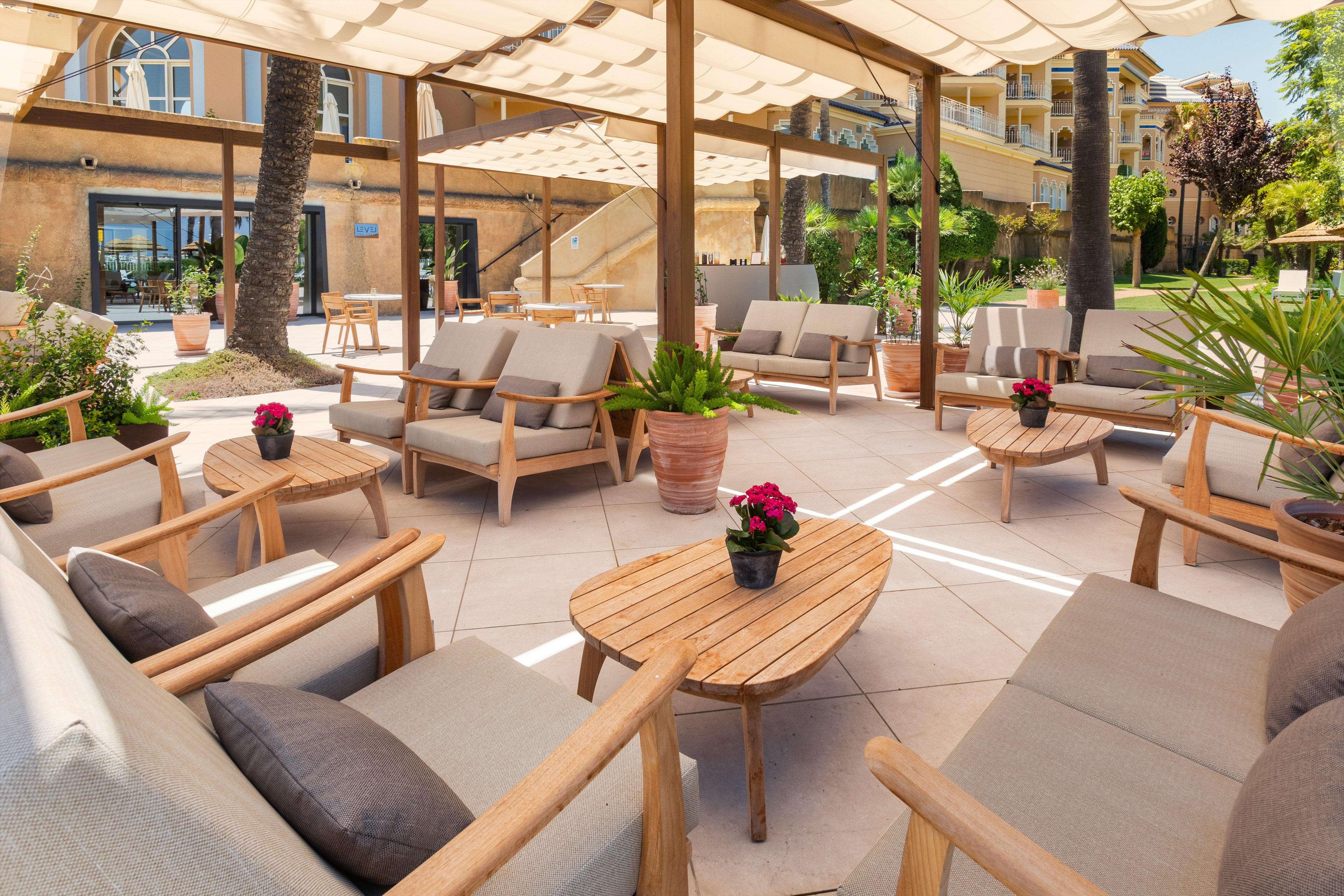 Hotel terrace lounge with shaded seating, wooden tables, and potted plants.