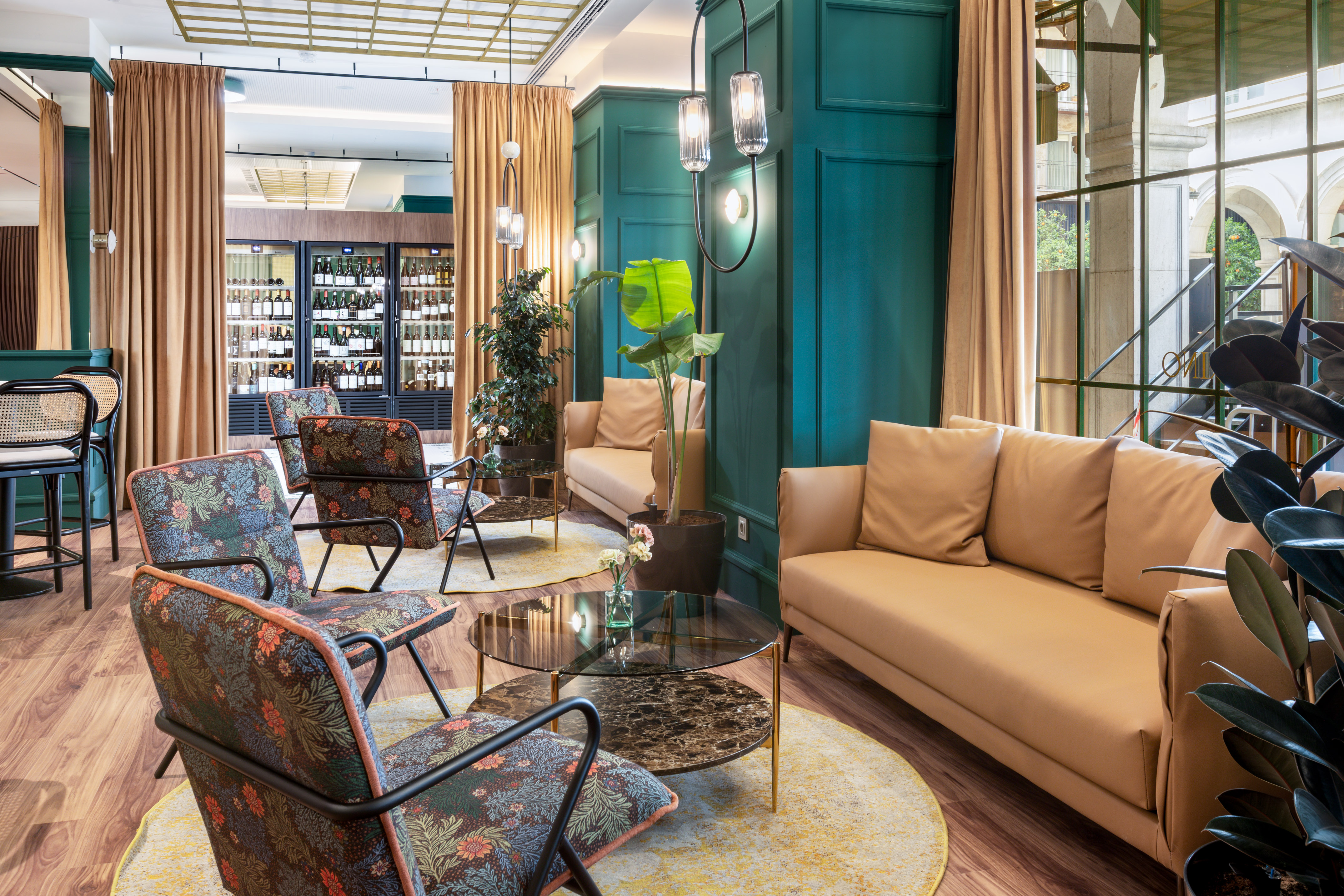 Teal-paneled hotel lounge with tan sofas, floral chairs, and wine display.