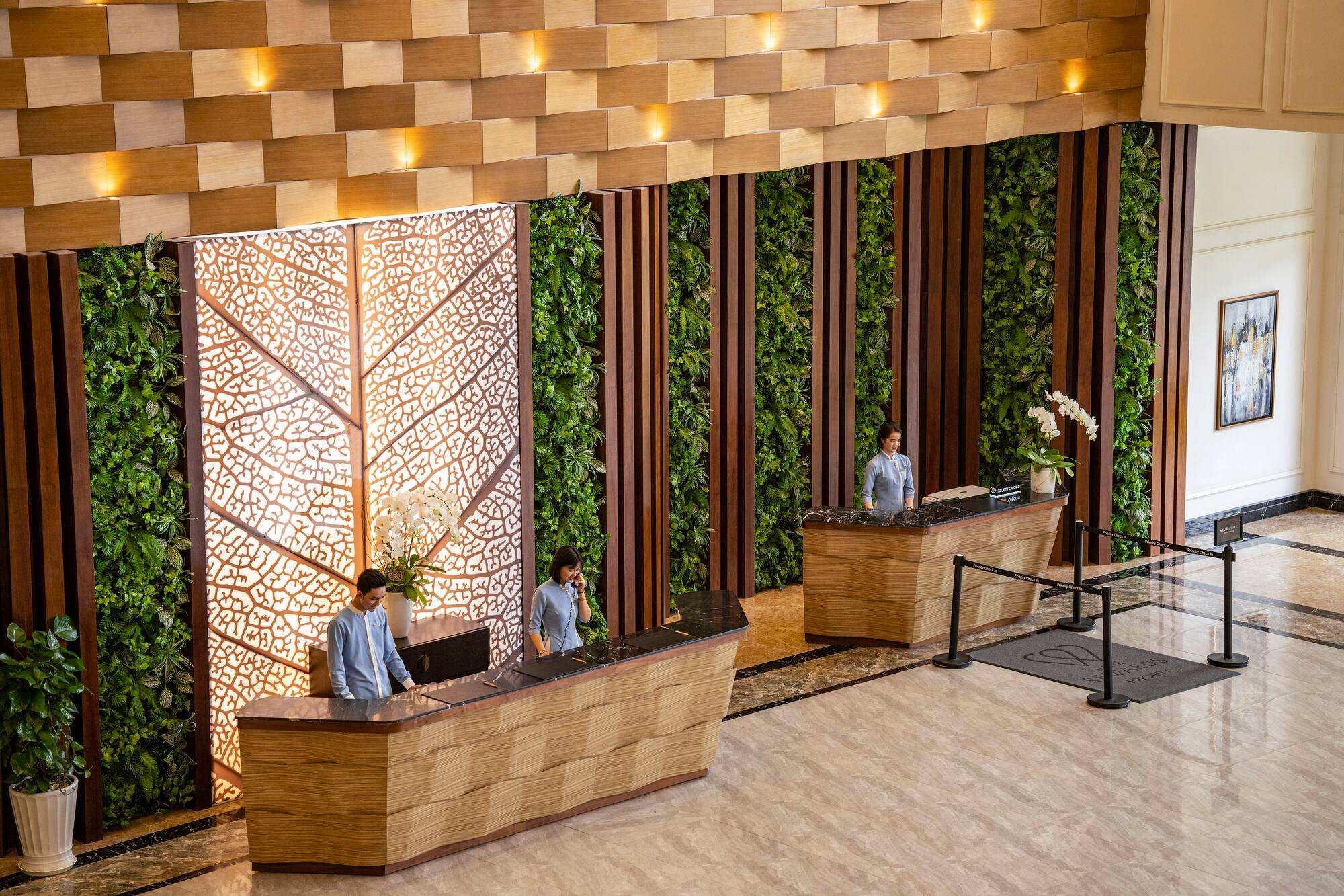 Modern hotel reception with living green walls, wood panels, and staff.