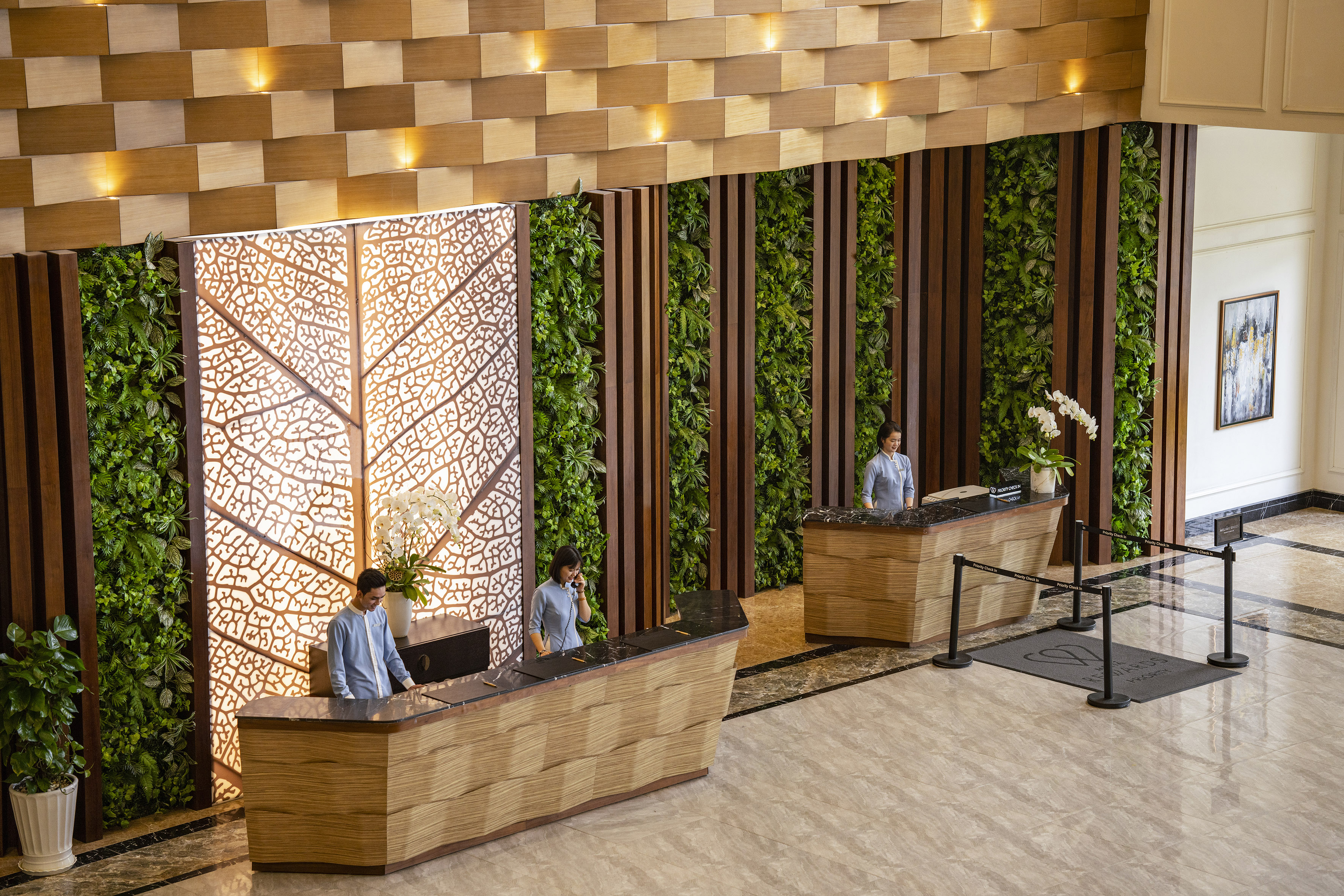 Modern hotel reception with living green walls, wood panels, and staff.