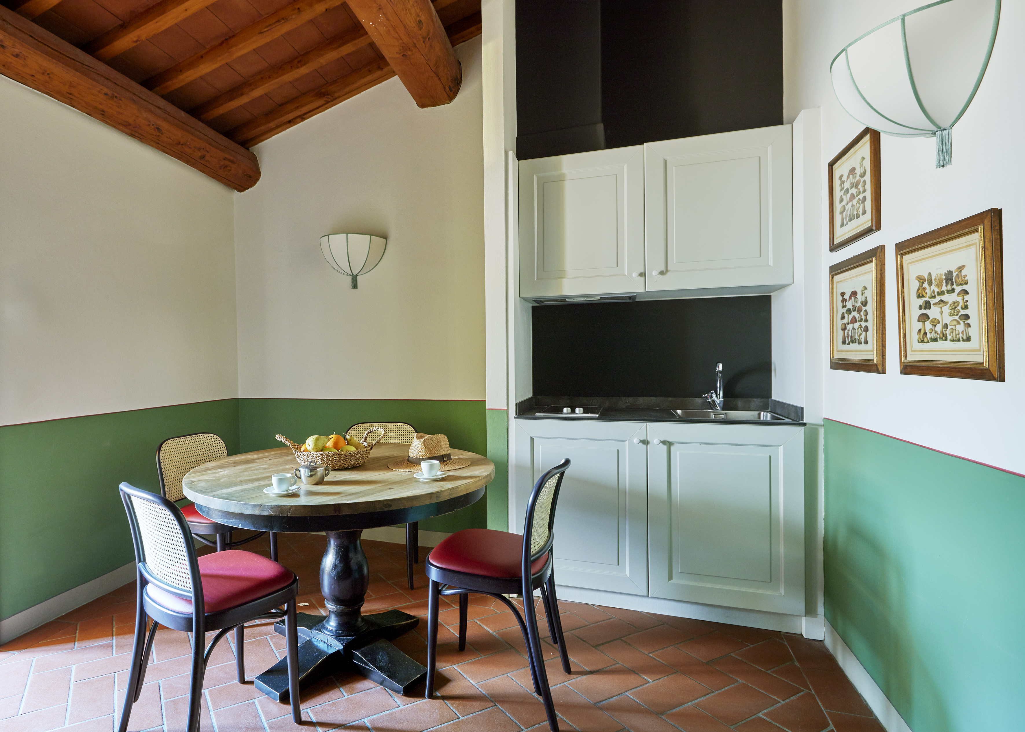 Cozy studio dining area with kitchenette, terracotta floor, and wood beams.