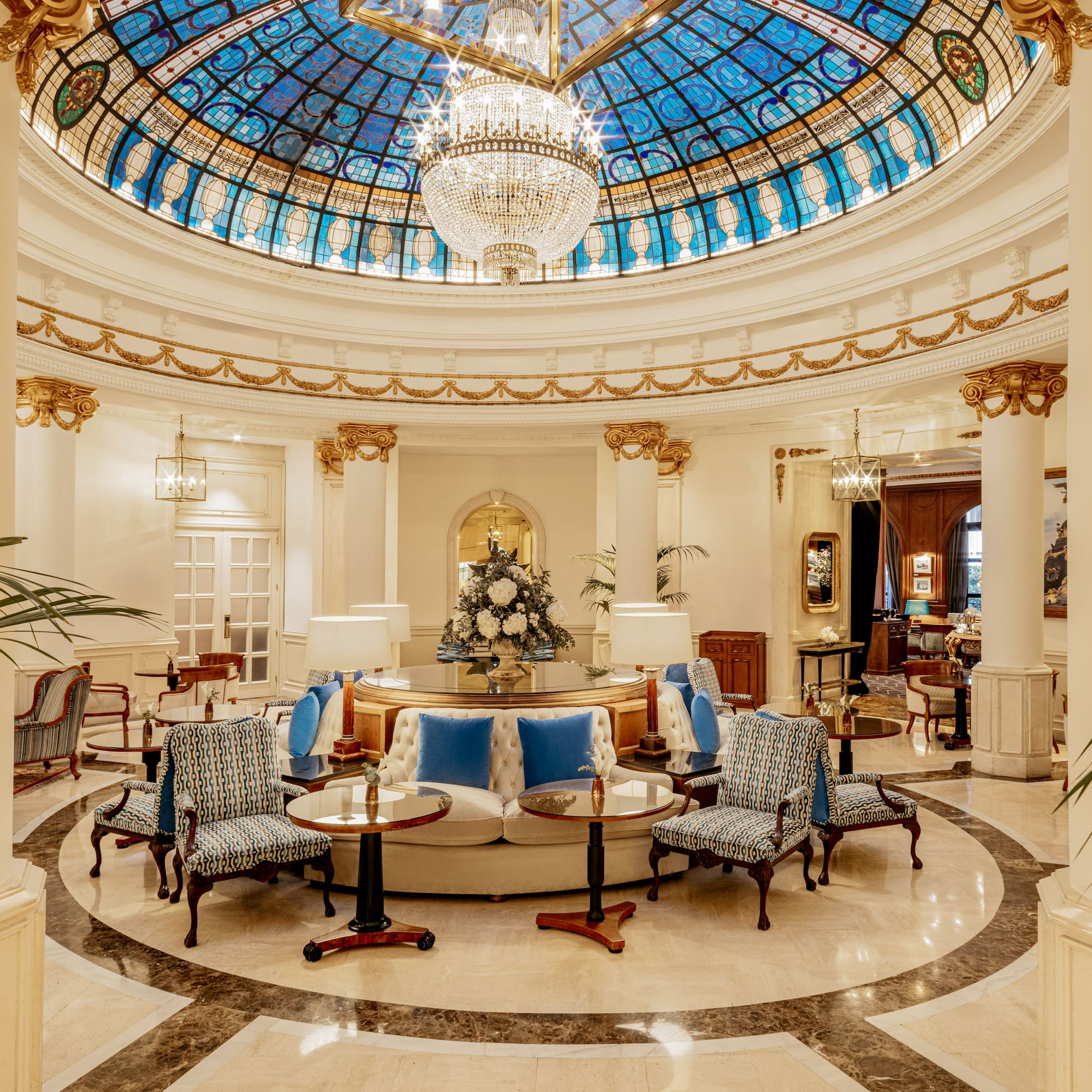 Elegant hotel lobby featuring a stained glass dome, crystal chandelier, and luxury seating.