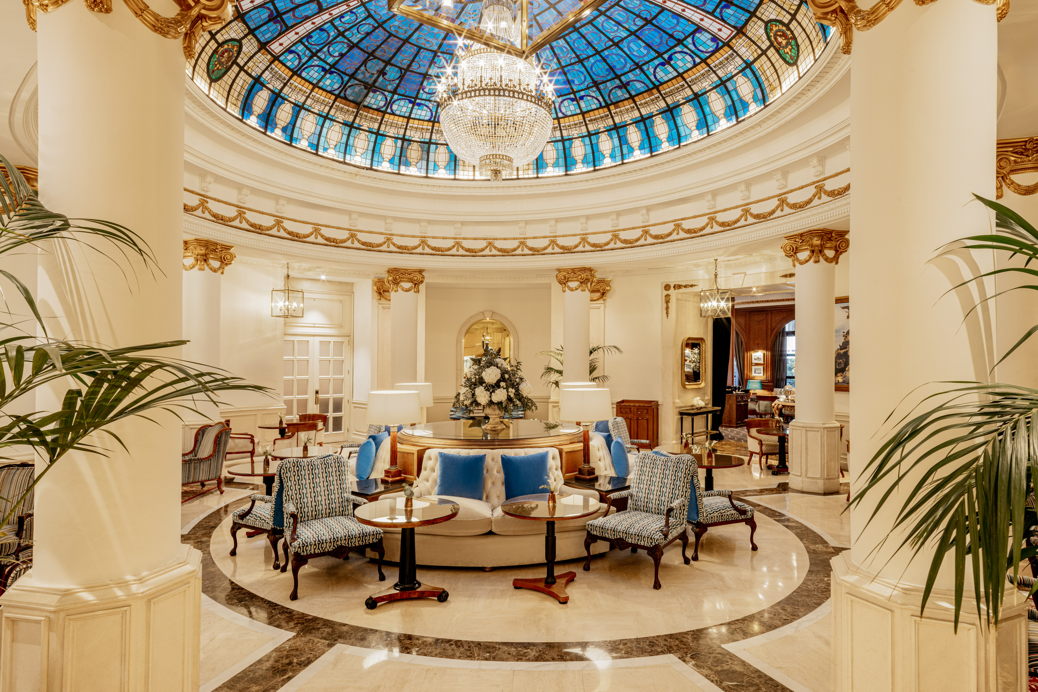 Elegant hotel lobby featuring a stained glass dome, crystal chandelier, and luxury seating.
