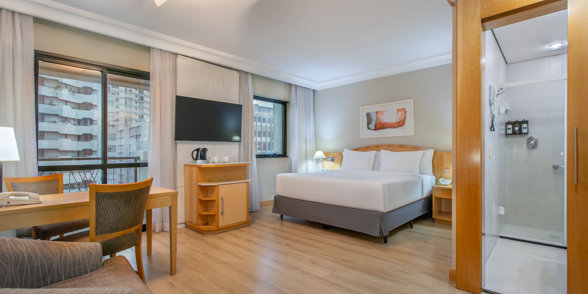 Modern hotel suite with king bed, desk, city view, and shower.