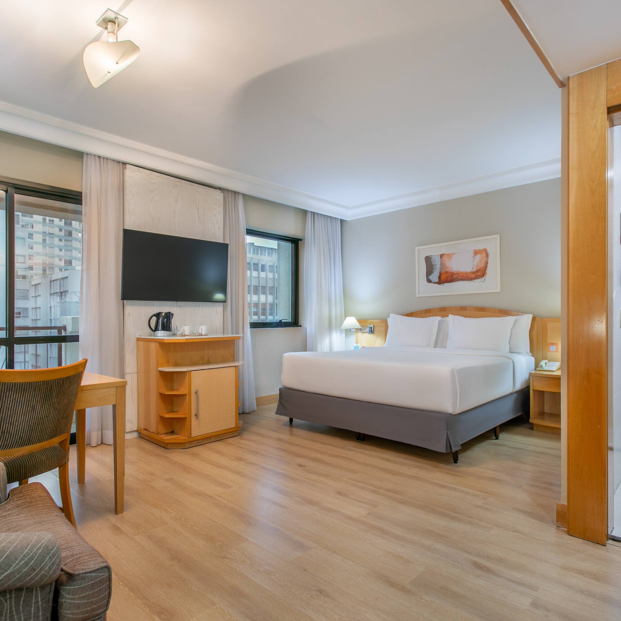 Modern hotel suite with king bed, desk, city view, and shower.