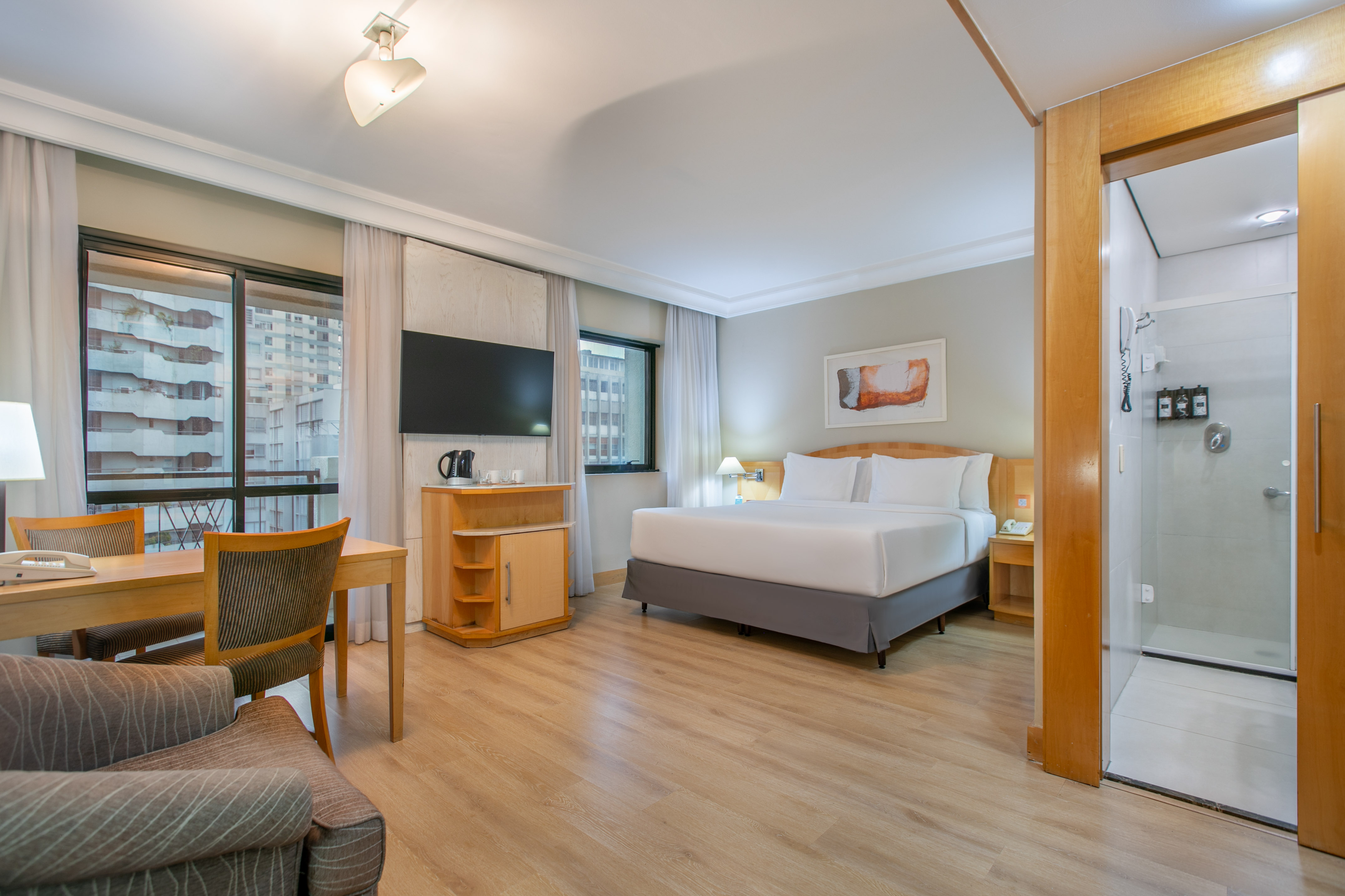 Modern hotel suite with king bed, desk, city view, and shower.