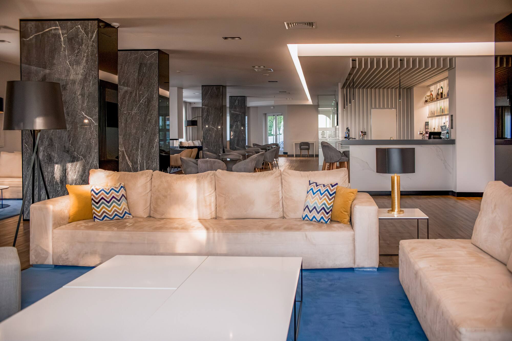 Modern hotel lobby with comfortable beige sofas, blue rug, and a sleek bar.