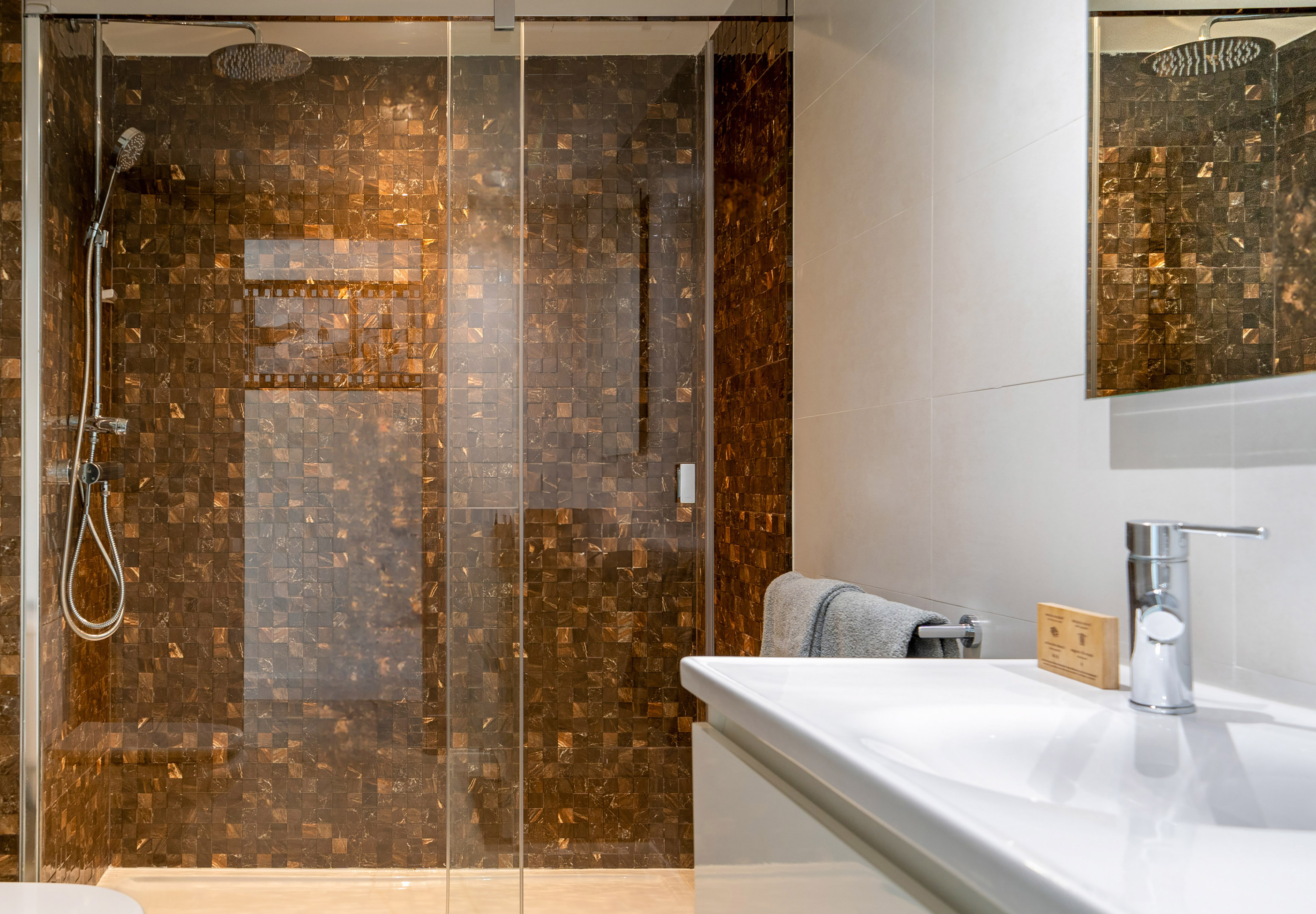 Modern bathroom with mosaic shower, rainfall head, white sink and faucet.